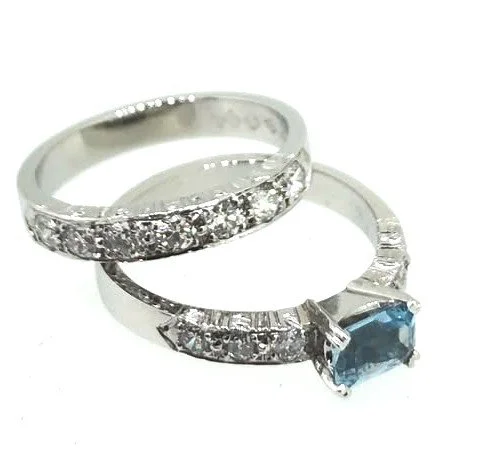 Two white gold rings, one with clear gemstones and one with a large blue gemstone, overlapping each other.