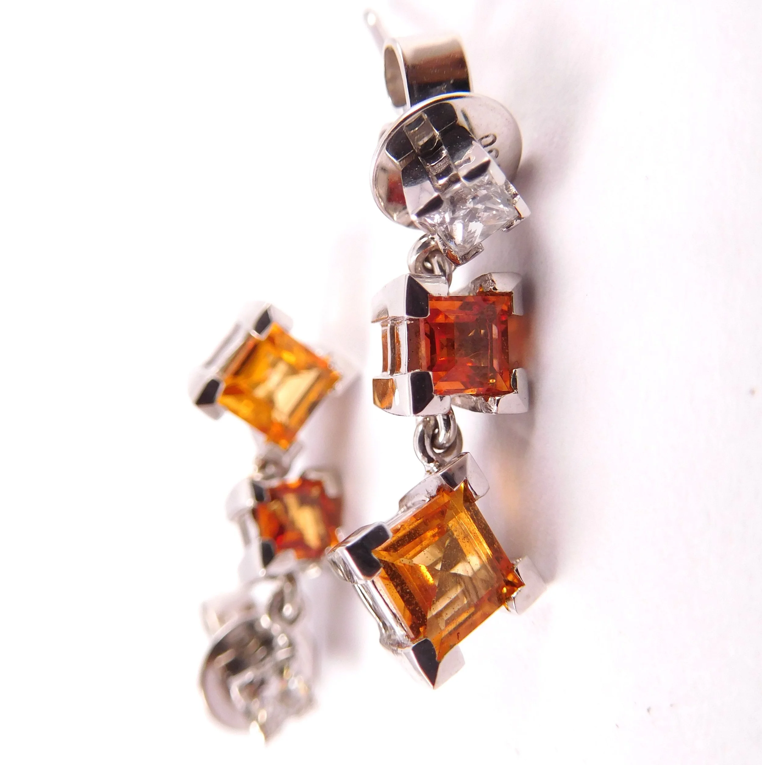 Close-up of a piece of jewelry with multiple orange and clear gemstones set in a silver metal setting.