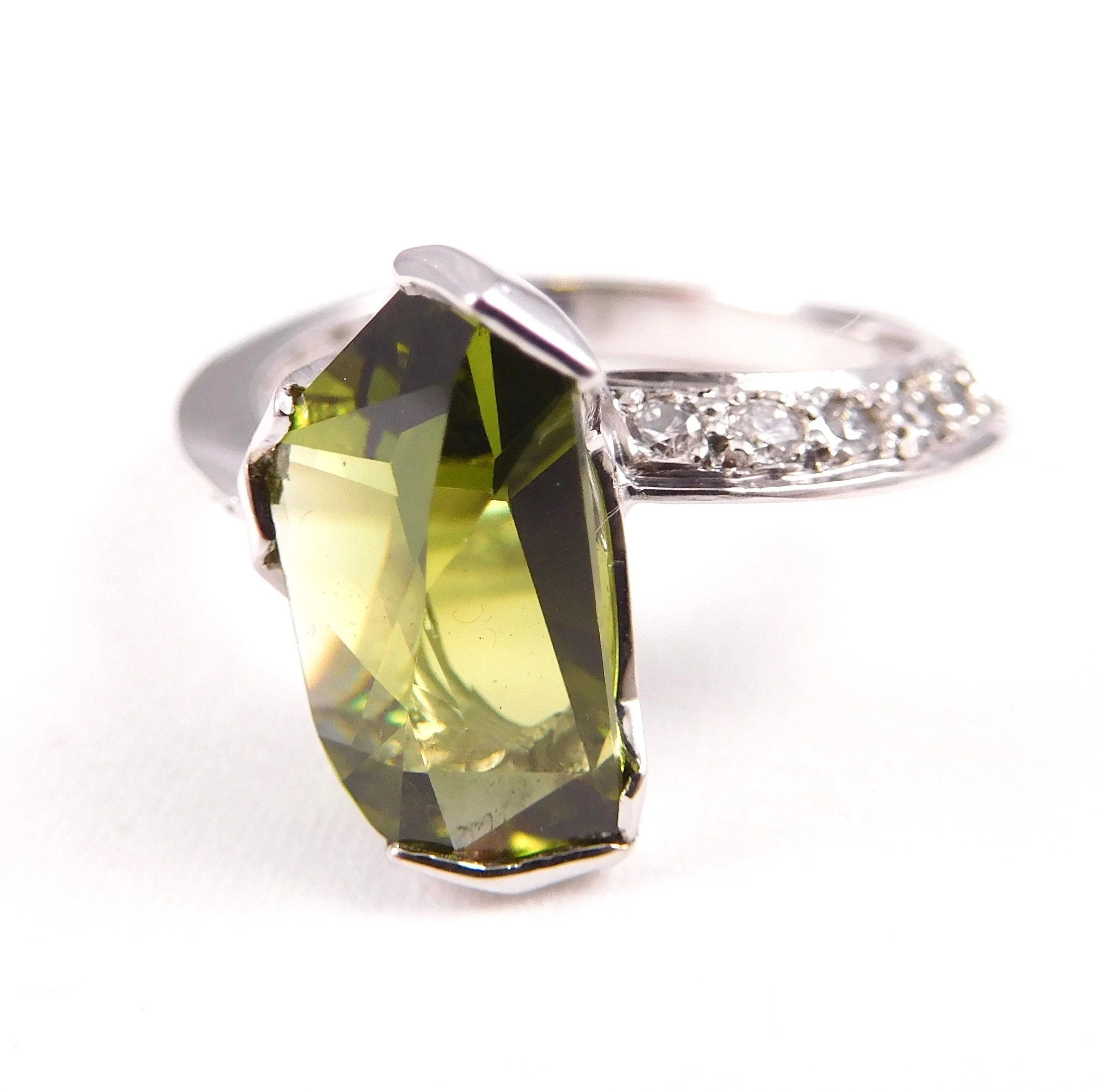 A close-up of a faceted gemstone with a yellow-green hue, showing its shine and cut details.