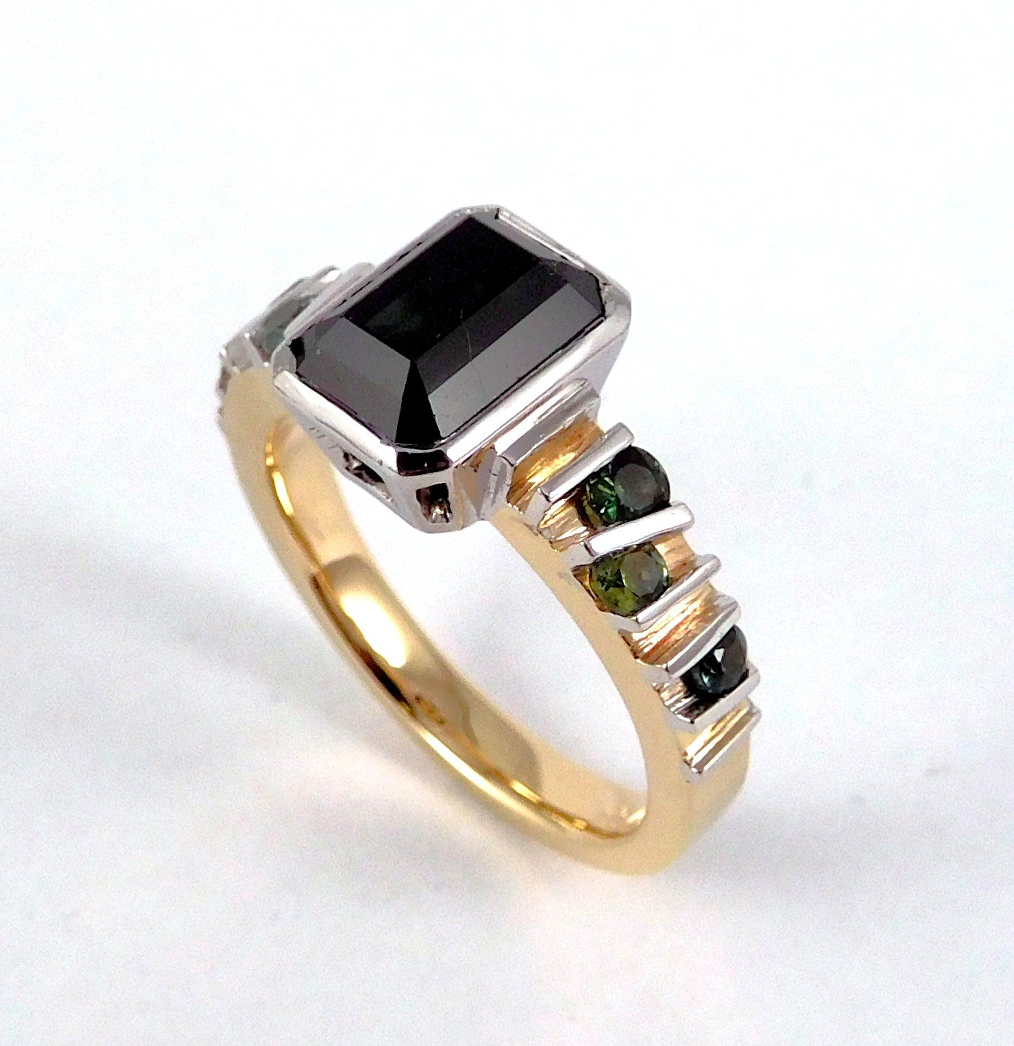 A gold ring with a large rectangular black gemstone on top and small round black and green gemstones set along its band.