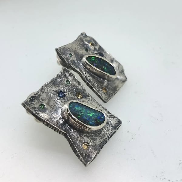 Silver earrings with large oval opal stones and small colored gemstones on a white background.