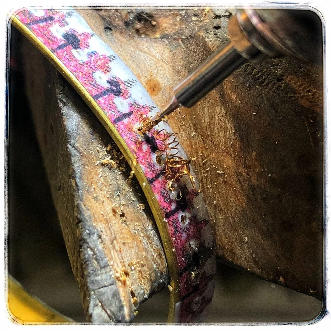A close-up of a gold band being drilled and formed, whilst supported by a wooden surface.