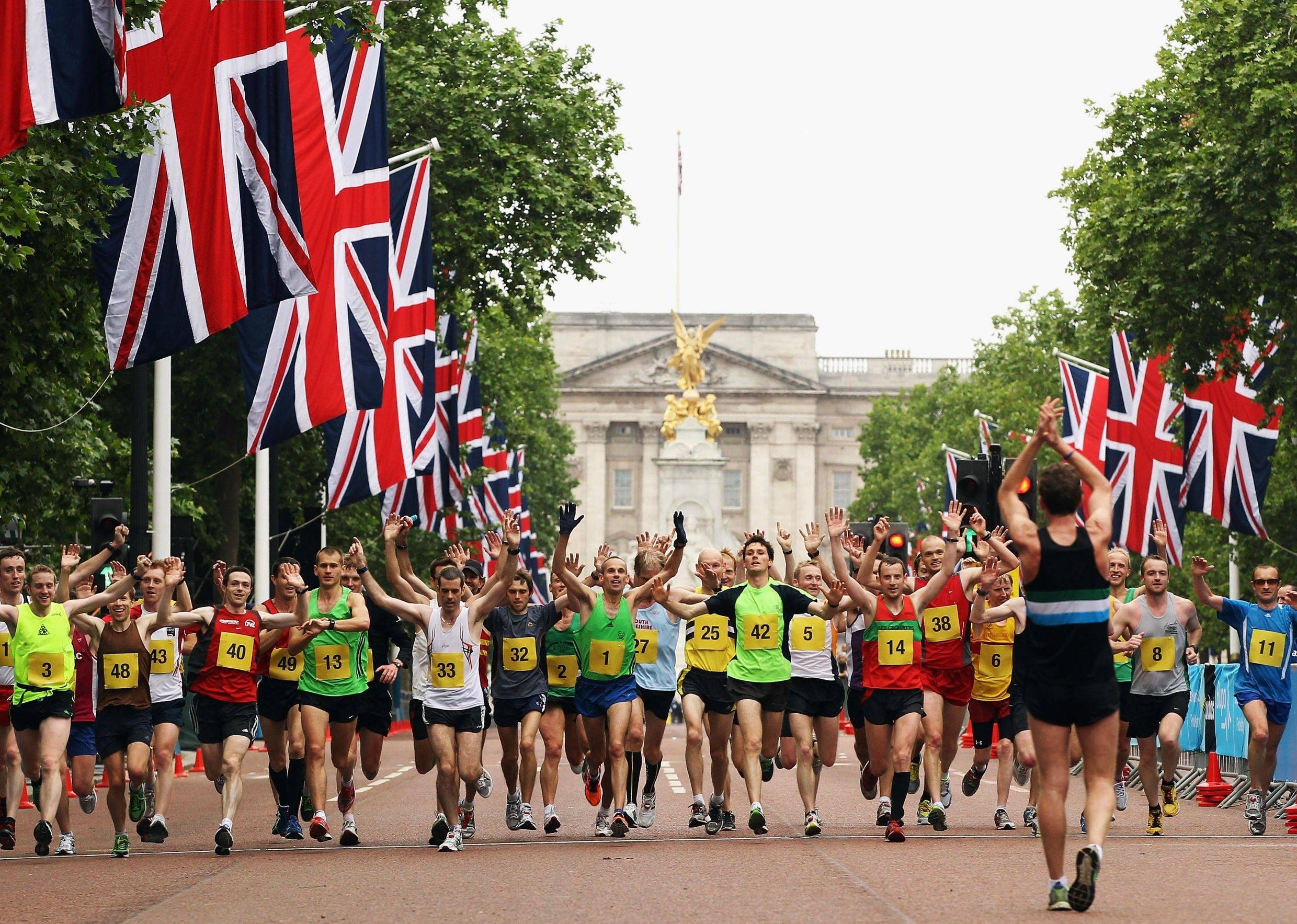 A large group of runners starting a race, with British flags lining the street and a historic building in the background.