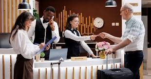 A man at a hotel reception desk handing a key card to a woman employee, with additional staff and a clock in the background.