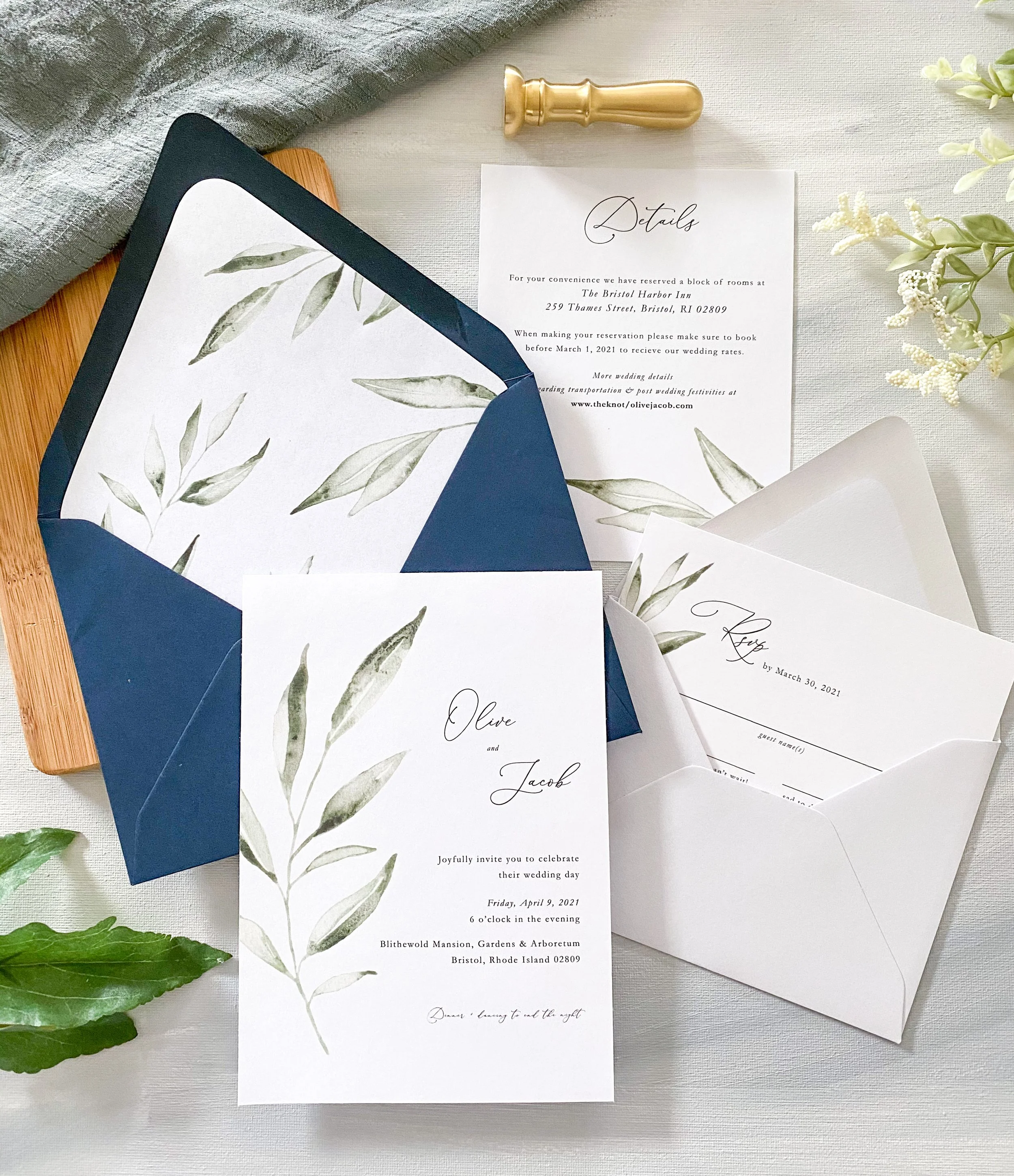 Wedding invitation suite with botanical design, including RSVP cards, details card, and envelopes, decorated with green foliage and a gold wax seal stamp.