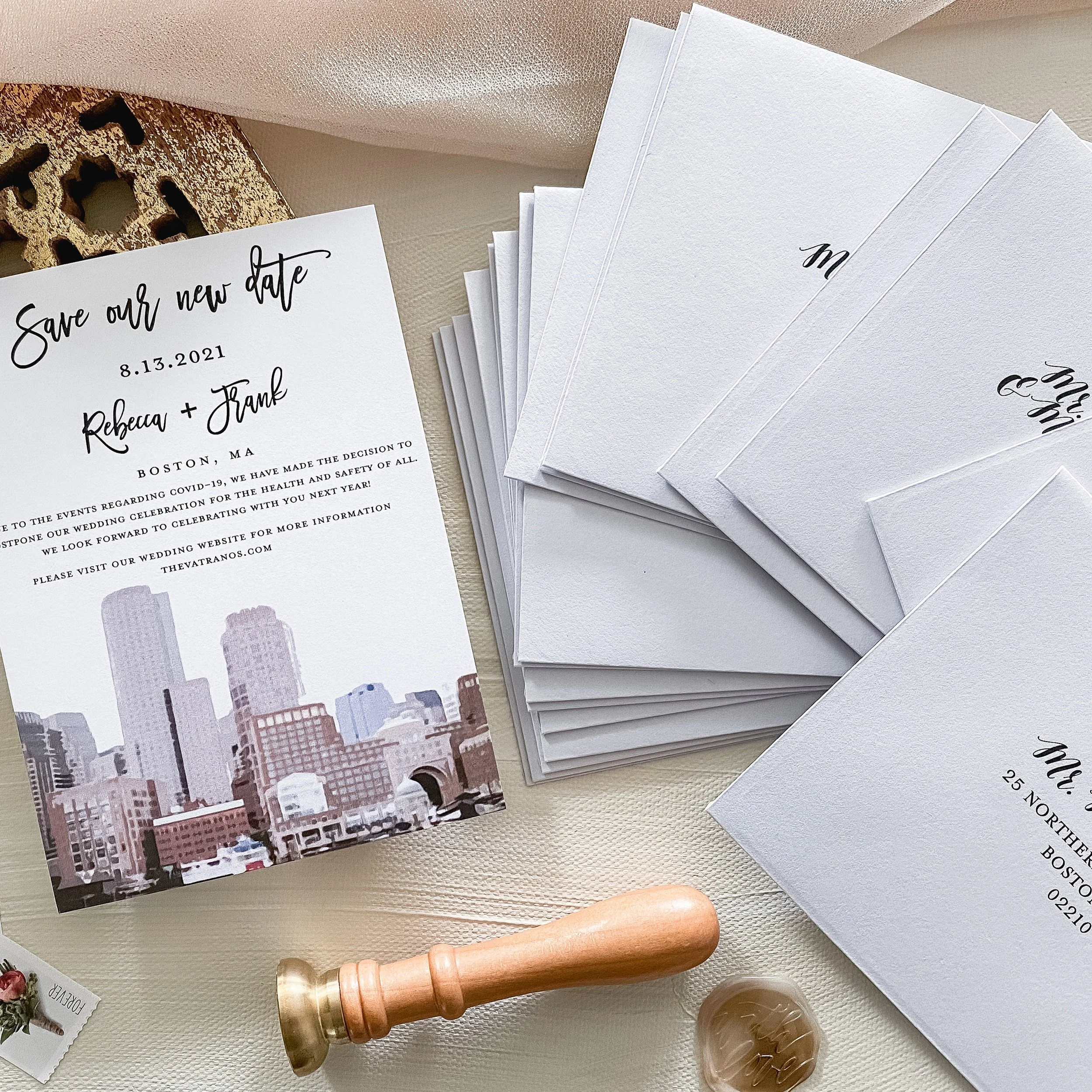 Wedding invitation with Boston city skyline, coordinating envelopes and sealing wax stamp on a light-colored surface.