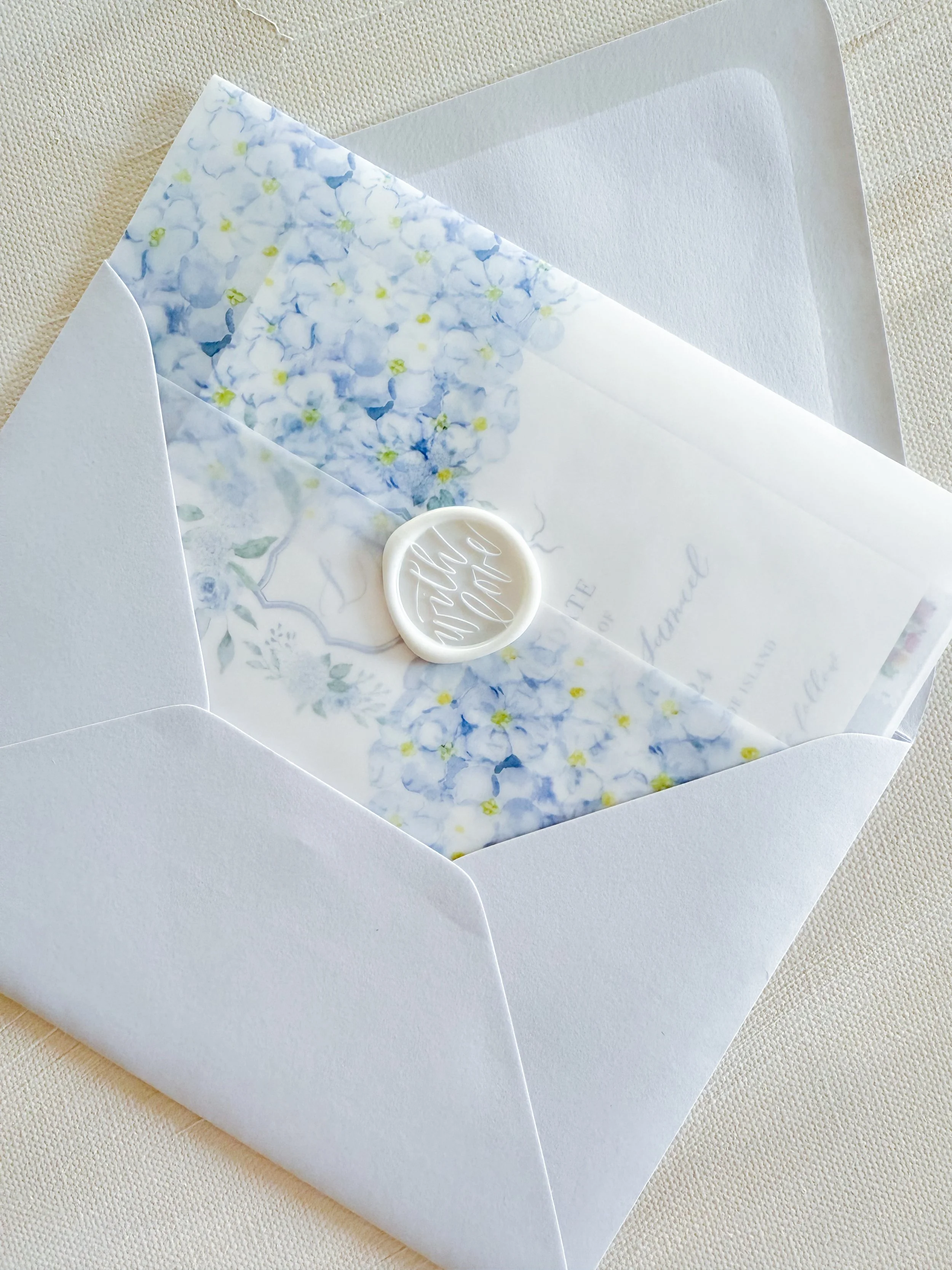 Close-up of a soft french blue euro flap envelope with a vellum white wax seal. A Custom Wedding Stationery Suite featuring blue hydrangea flow printed vellum wrap with Invitation, Details Cards, RSVP assemble inside.