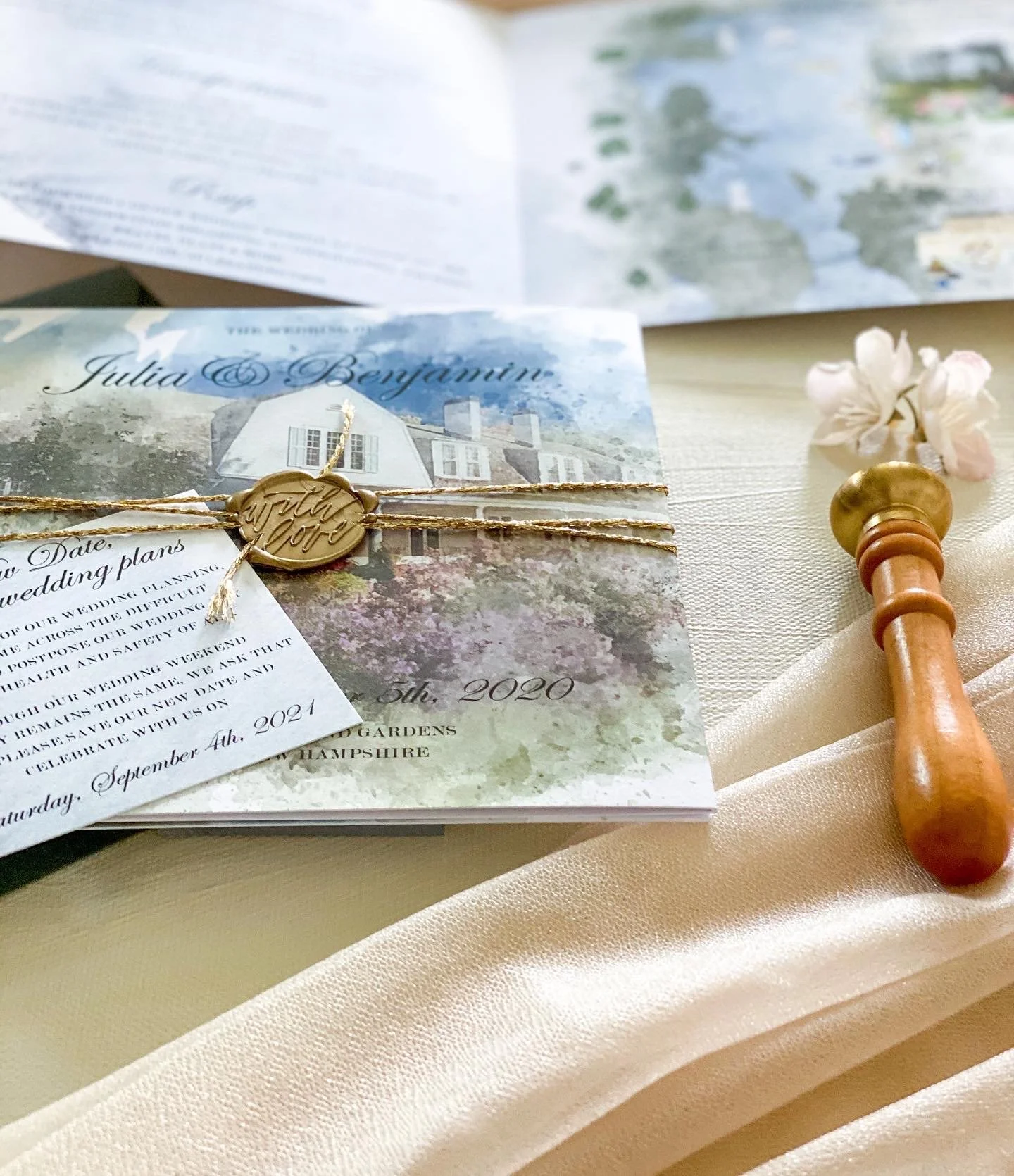 Wedding invitation with gold seal and twine, gold stamp that says Bride and Groom, couples name, and a wooden wax seal stamp on a white fabric surface.