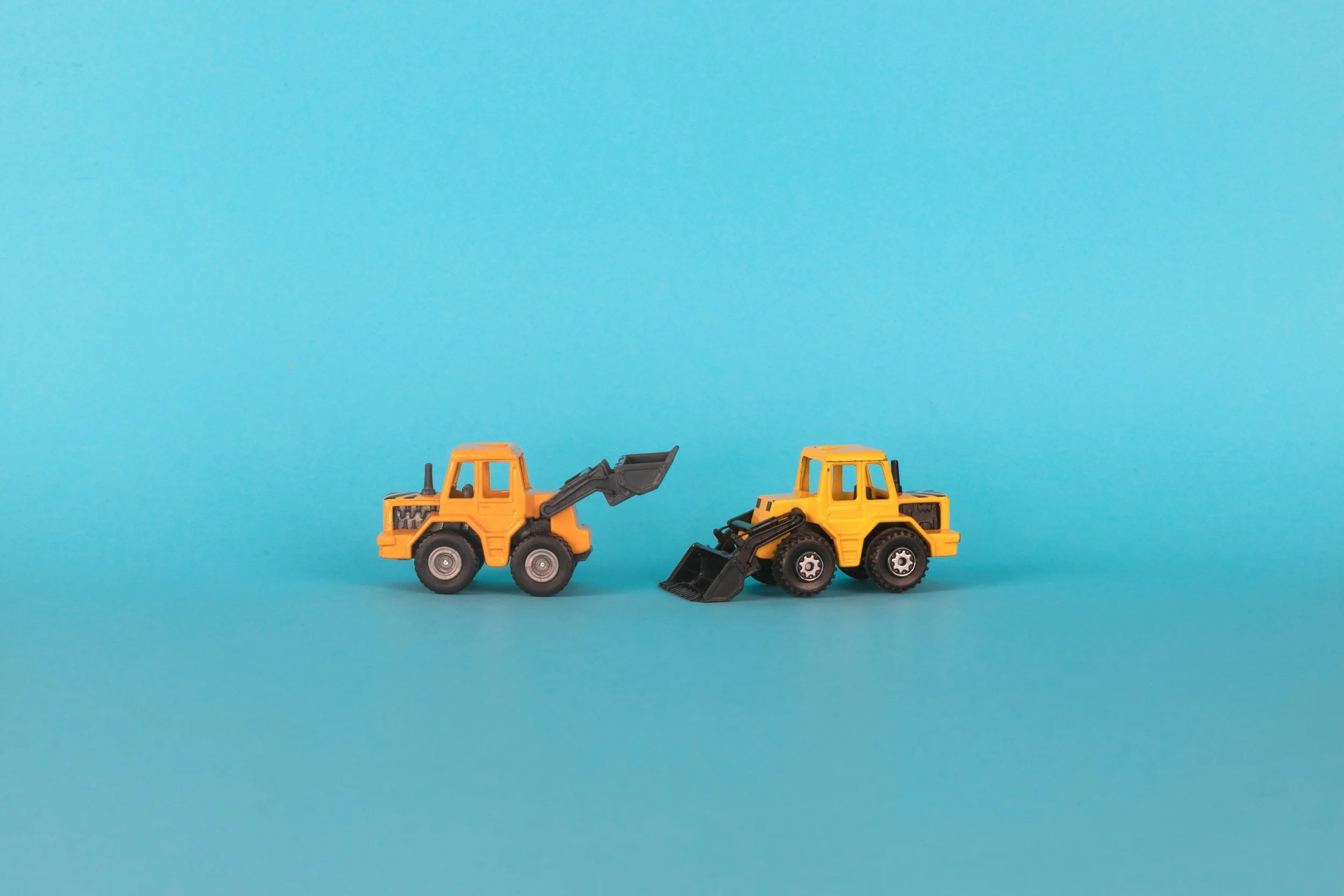 Two small yellow toy construction vehicles with black parts against a blue background.