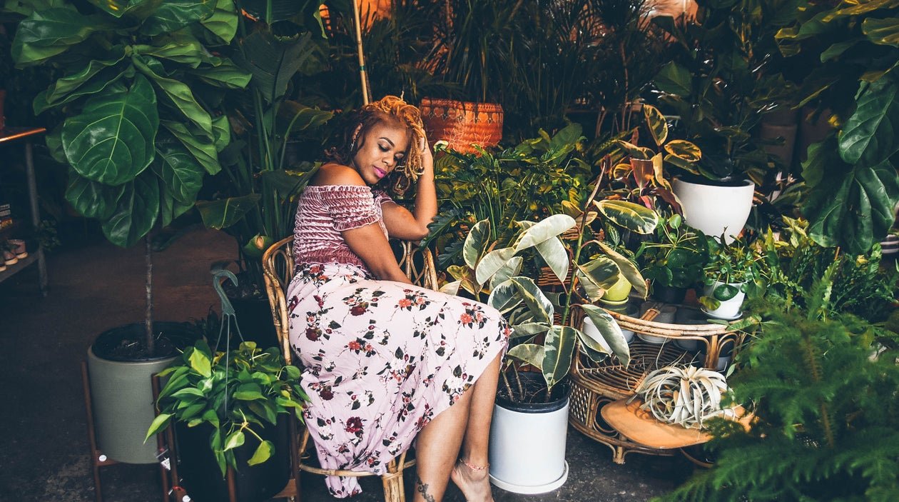 Black woman in pink dress sitting in a chair surrounded by lush plants