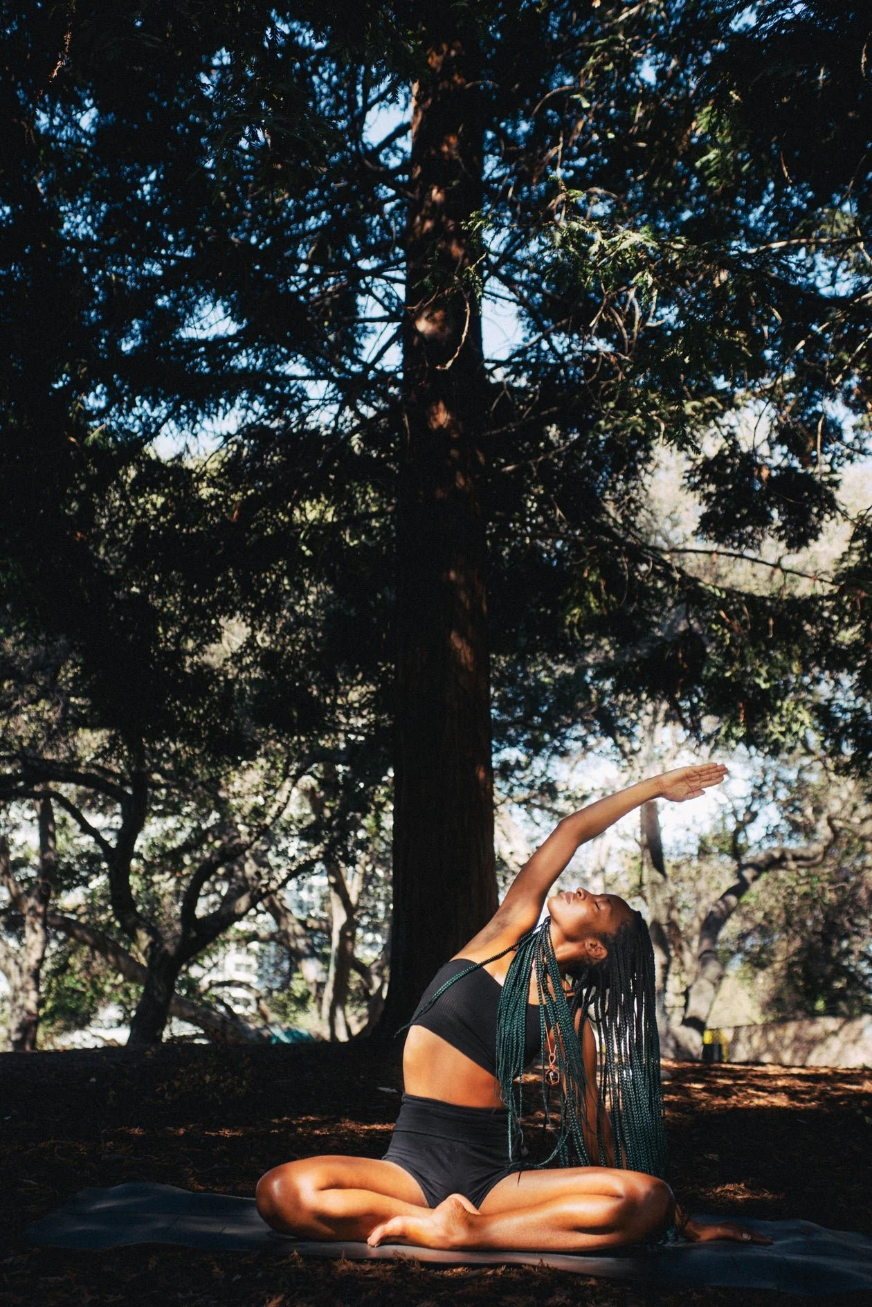 Black woman sitting and stretching on the ground in front of a tree