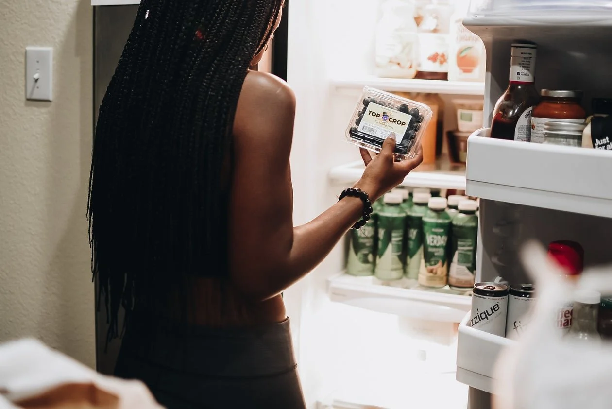 Black woman standing in front of an open fridge holding berries