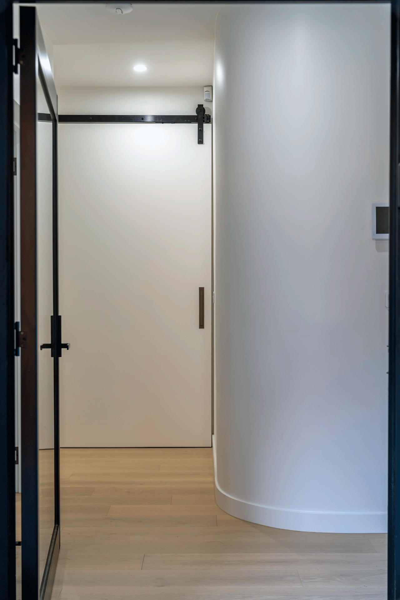 Unique curved wall in the entranceway of modern renovation with barn door style bedroom door