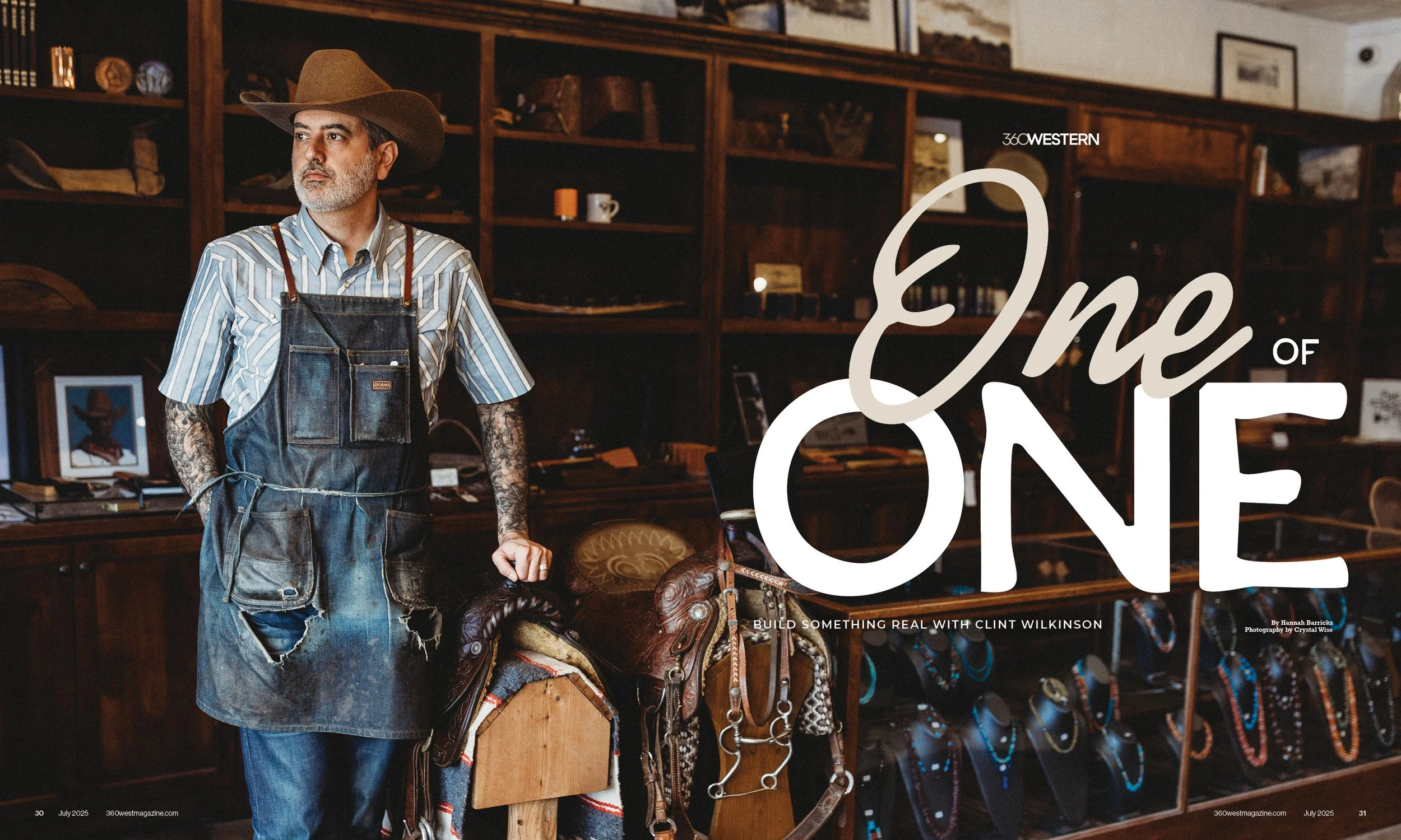 A man with tattoos wearing a cowboy hat, striped shirt, and apron standing in a room with wooden shelves and jewelry displays