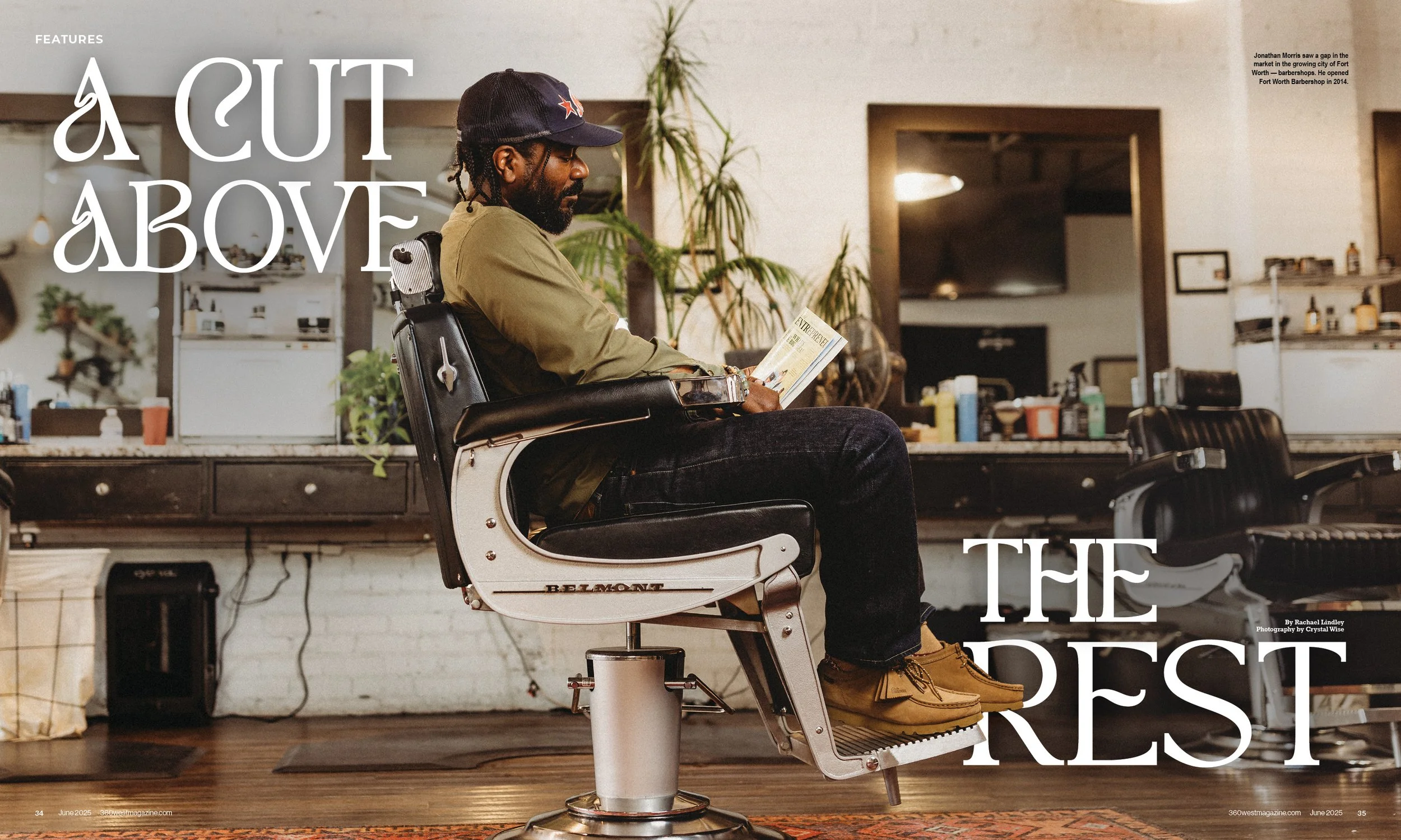 A man with dreadlocks sitting in a vintage black barber chair reading a magazine in a barbershop, with plants and various grooming products on shelves and counters surrounding him.