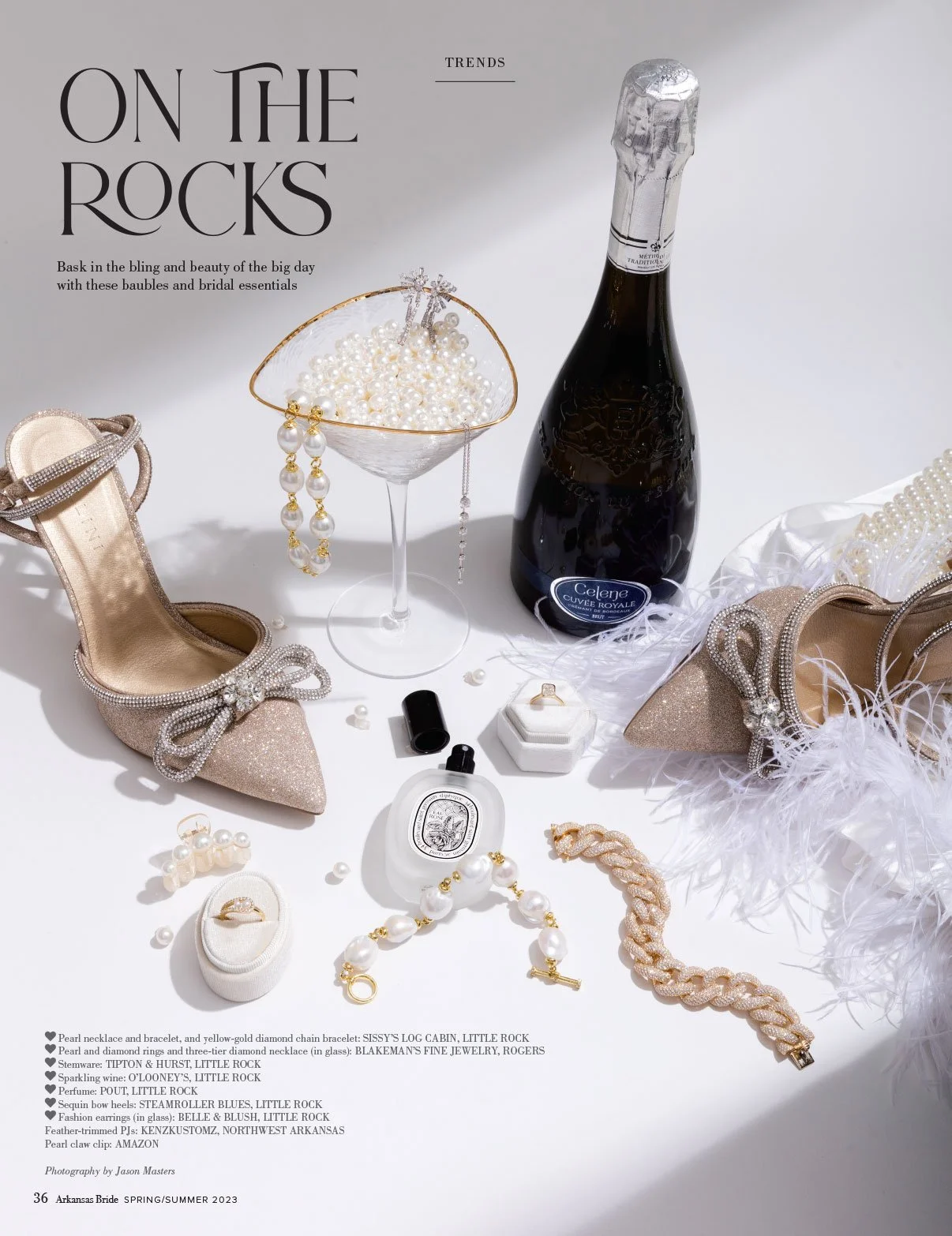 Display of jewelry, shoes, champagne, perfume, and accessories on a white surface, styled for celebration.