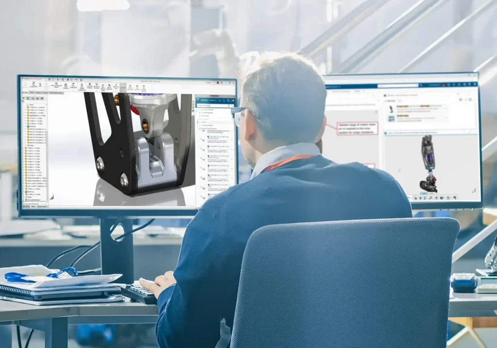 Person working on CAD design of a mechanical component with multiple monitors in an office setting.