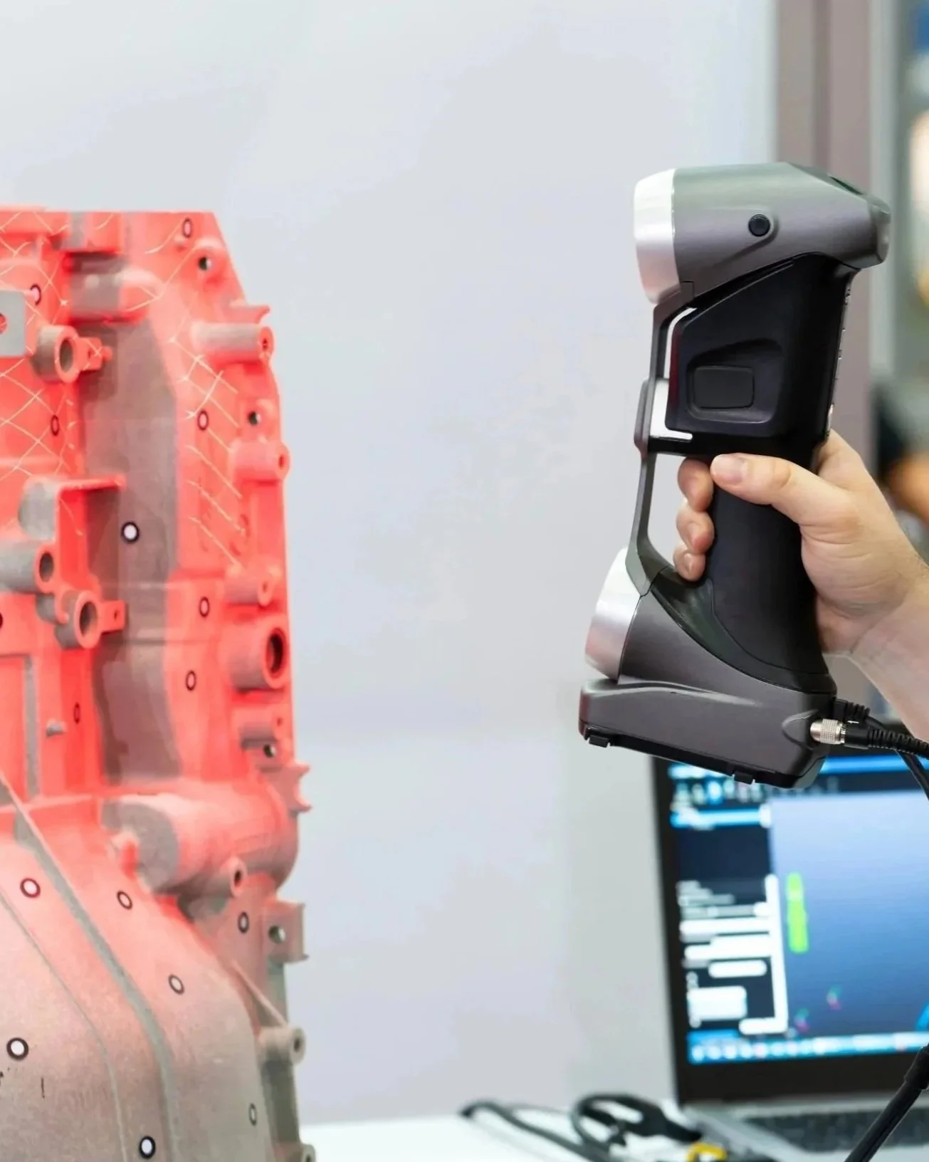 A person using a handheld scanner to examine a large pink and gray mechanical part connected to a computer with diagnostic software.