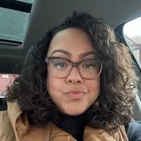 A woman with curly dark hair and glasses sitting in a car