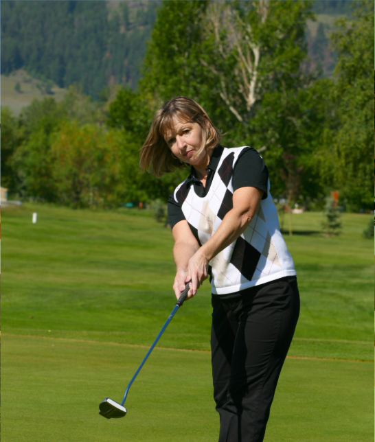 Woman golfing on a lush green course with trees and mountains in the background.