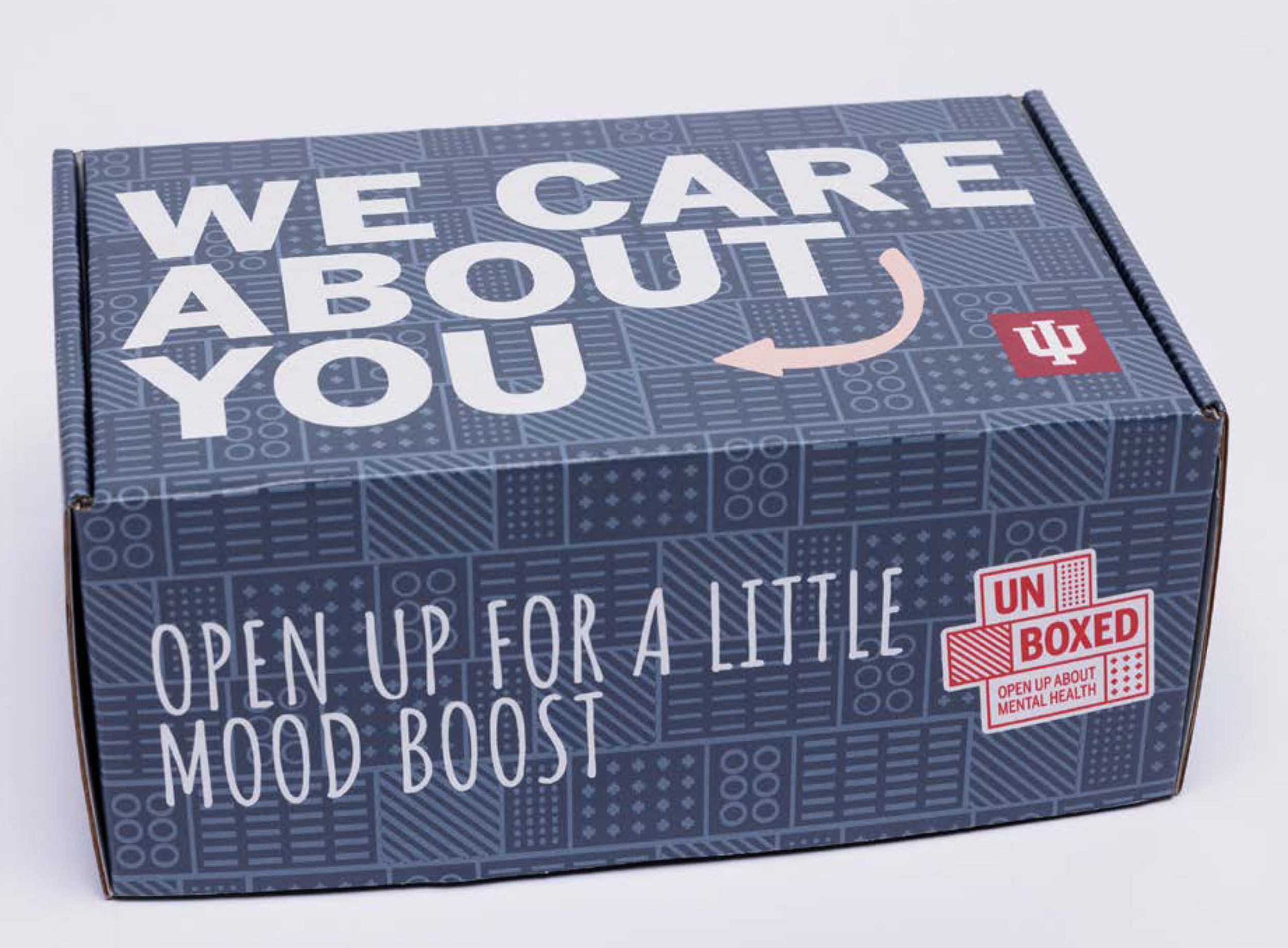 care package box with a blue tone on tone block pattern. Top reads We care about you. Front reads Open up for a little mood boost