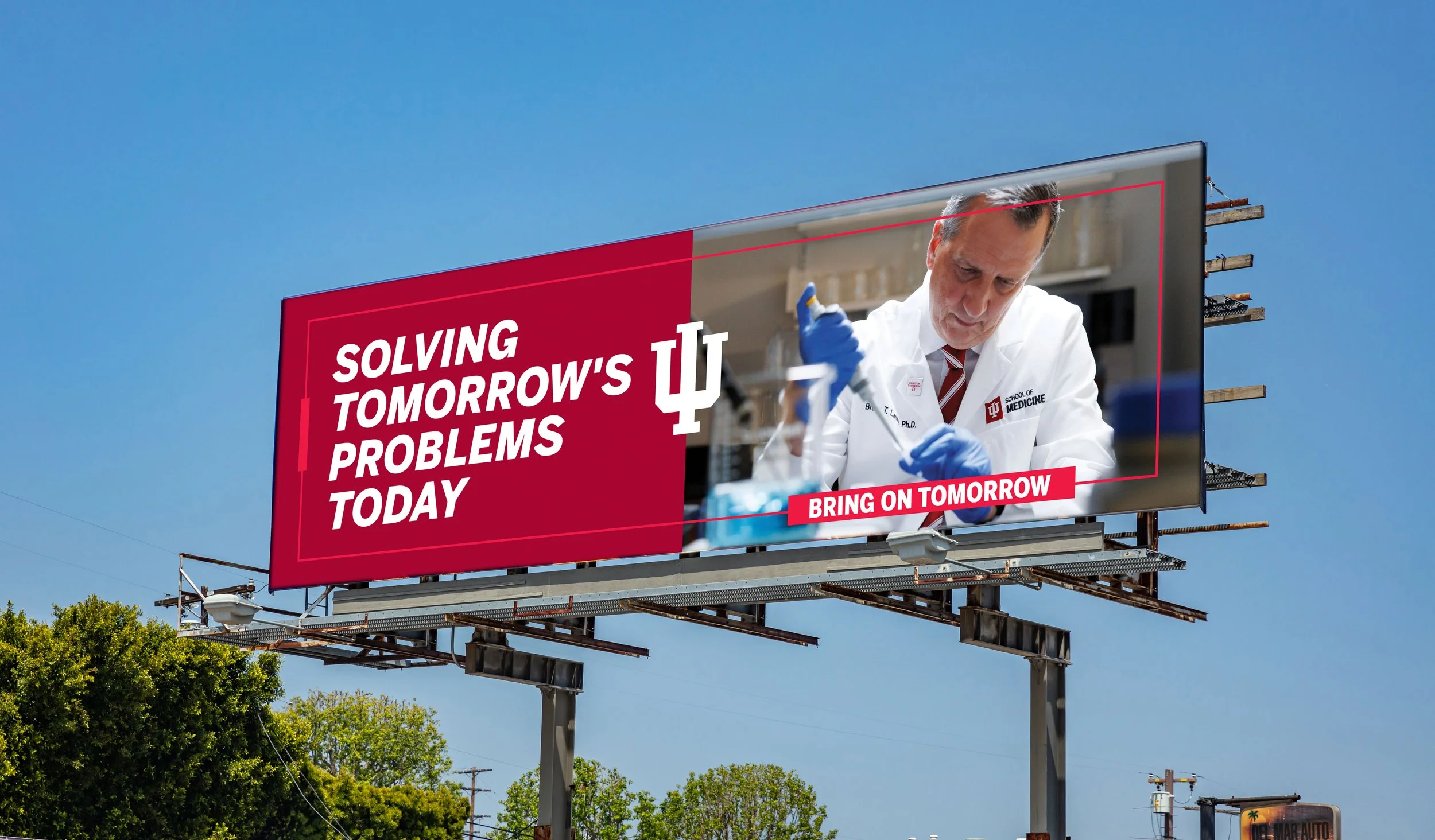 Billboard reading "Solving tomorrow's problems today" with a male scientist in a white coat and blue gloves working in a lab