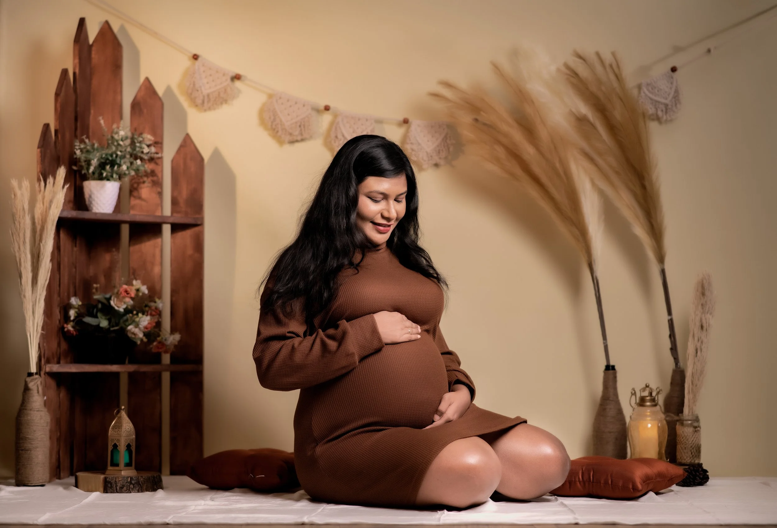 Pregnant woman sitting on the floor in a cozy, decorated room, cradling her belly and smiling gently.