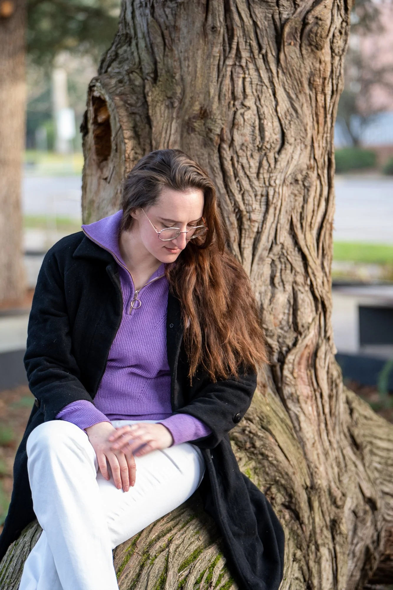 Congressional candidate Zeva Rosenbaum sits in front of a tree, wearing a purple sweater, black coat, and white pants.