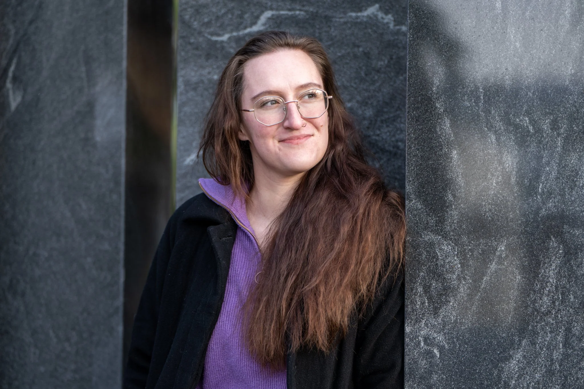 Congressional Candidate Zeva Rosenbaum stands in front of a gray stone background, smiling and looking to the right.