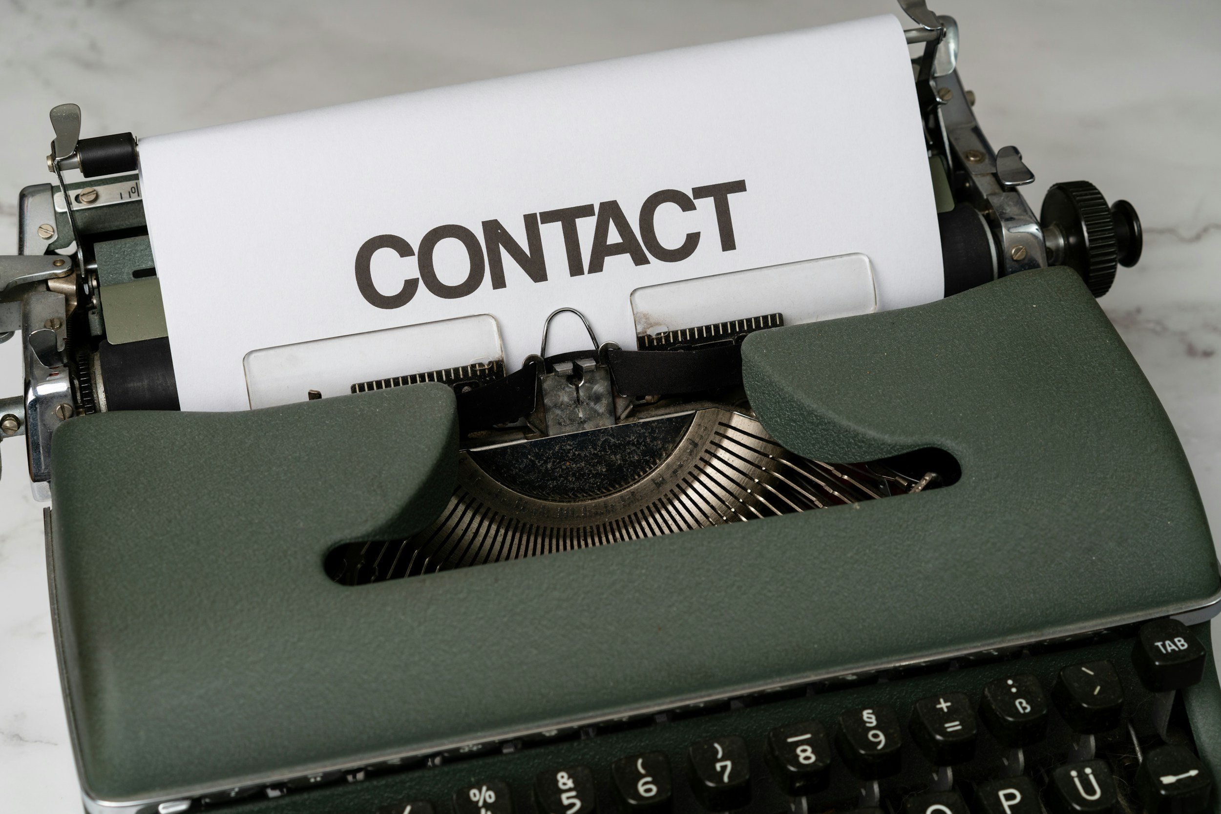 A vintage typewriter with a paper that says "CONTACT" in large bold letters.