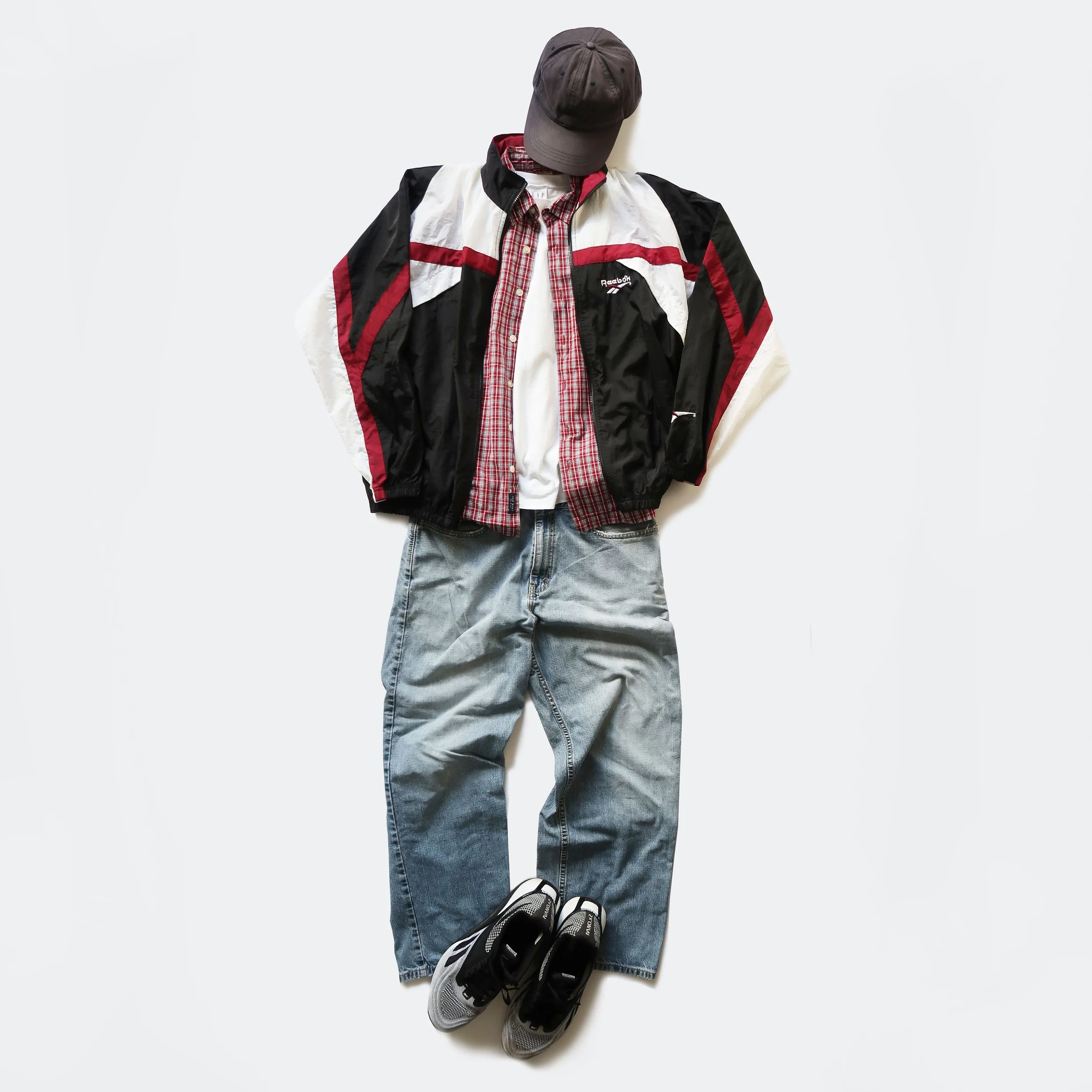 Casual streetwear outfit on a mannequin including a black and white jacket with red accents, a red and white checkered shirt, a white T-shirt, gray jeans, and black and white athletic shoes, with a dark baseball cap.