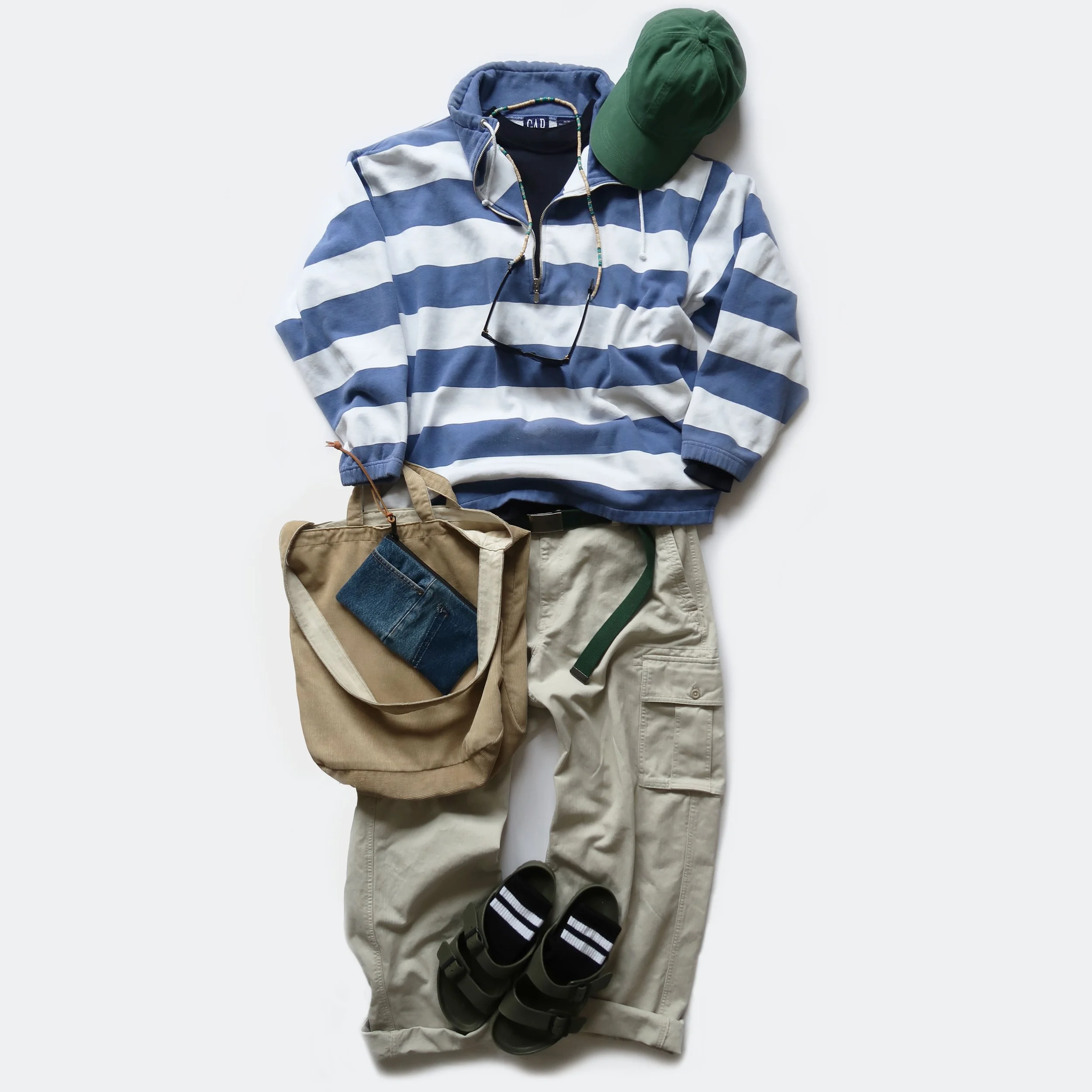 A laid-out outfit including a blue and white striped hoodie, khaki pants, black sandals, striped socks, a green cap, sunglasses, and a bag.