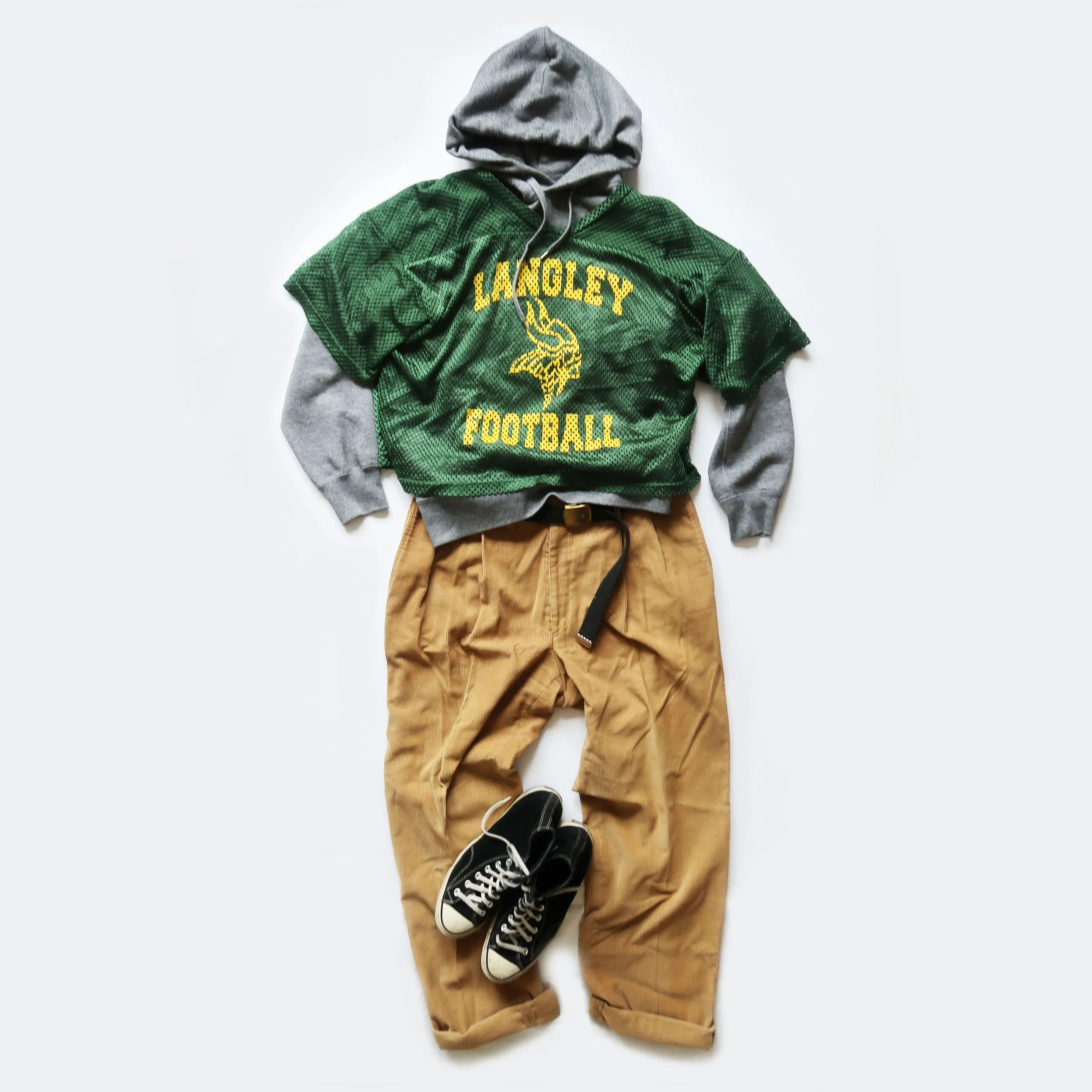 Casual outfit laid out flat, including a gray hoodie, a green football jersey with yellow lettering and a Viking head logo, tan pants, and black sneakers with white laces.