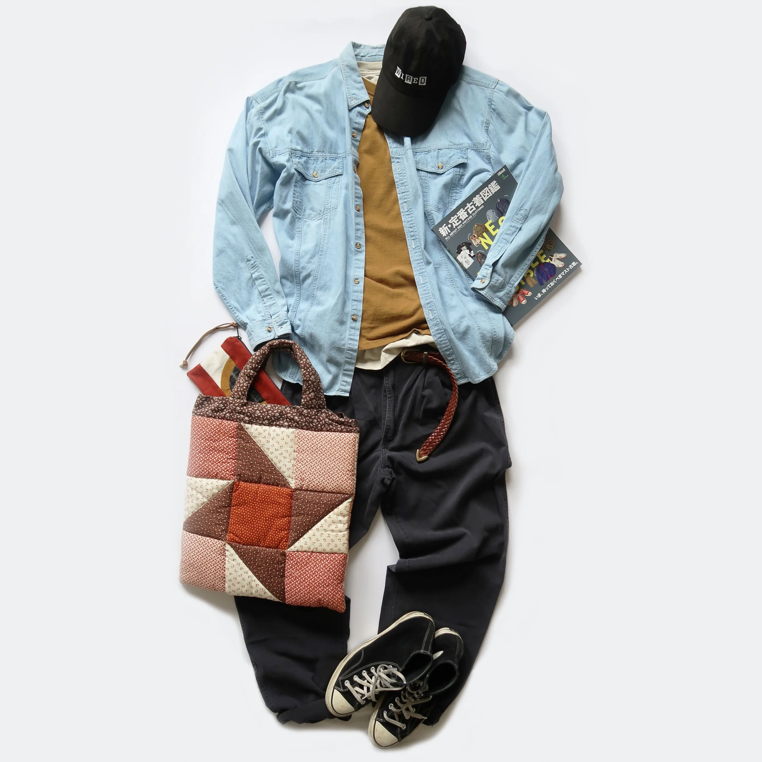 Casual clothing and accessories including a black cap, light blue denim jacket, tan T-shirt, plaid bag, black pants, and black sneakers with white soles, arranged on a white background.