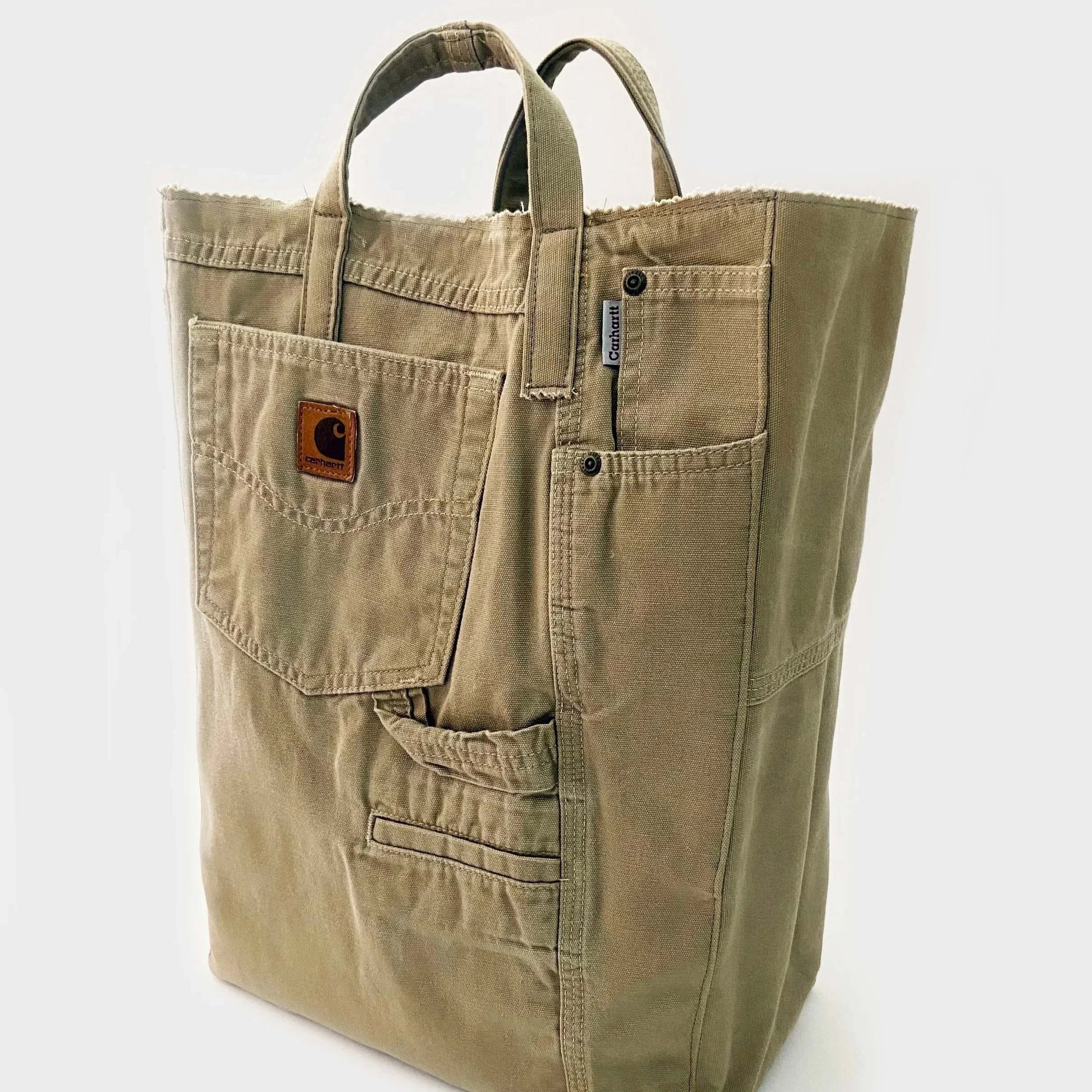 A tan tote bag made from a durable canvas material with dual handles, a front pocket, and a Carhartt label.