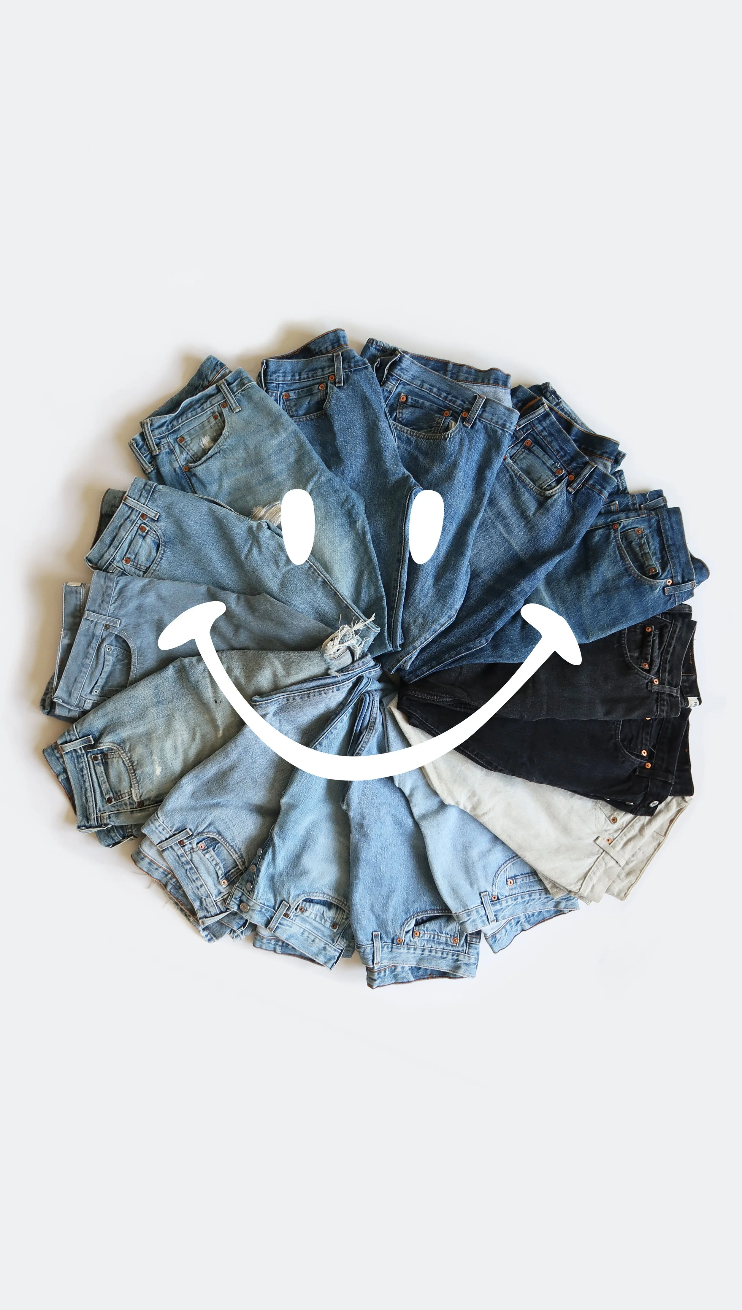 Circle of various shades of blue jeans arranged on a white surface with a white happy face drawn on it.