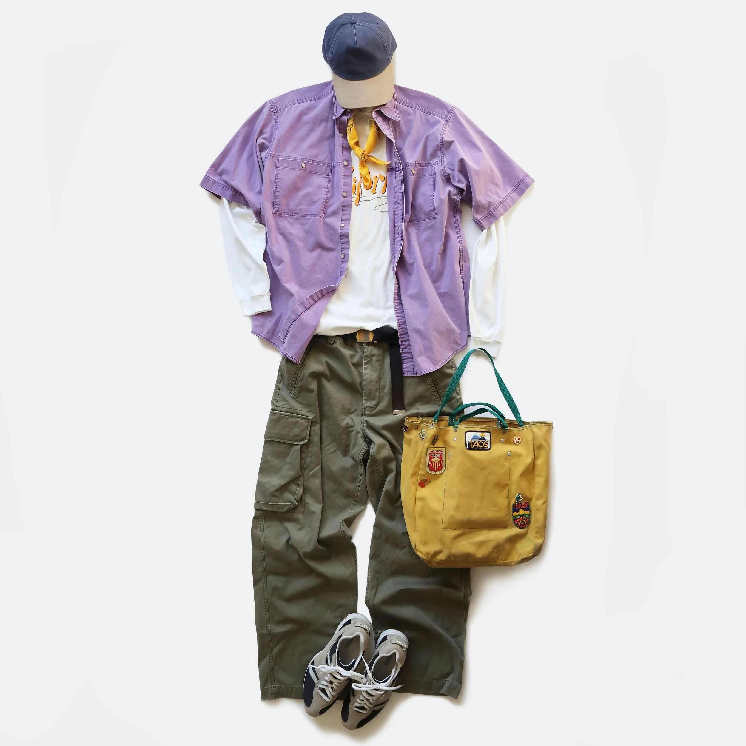 Casual outfit laid out on a white background, including a purple short-sleeved button-up shirt, a white graphic t-shirt, dark green cargo pants, gray sneakers, a baseball cap, a yellow bag, and a yellow bandana.
