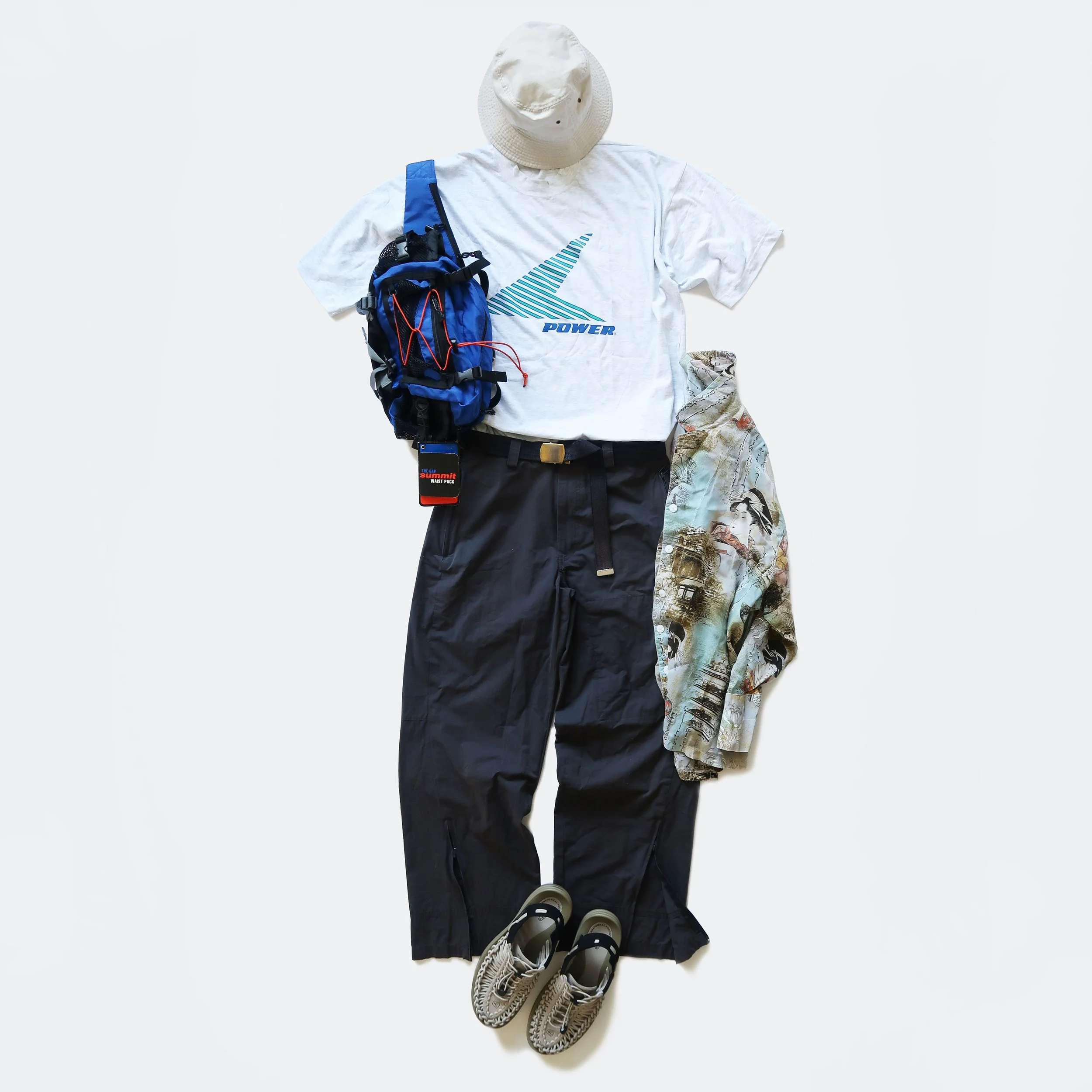 Casual outdoor outfit includes a white bucket hat, a white t-shirt with a blue and teal graphic and the word 'Power', black pants, beige sneakers, a blue backpack with red straps, and a map, all arranged on a white background.