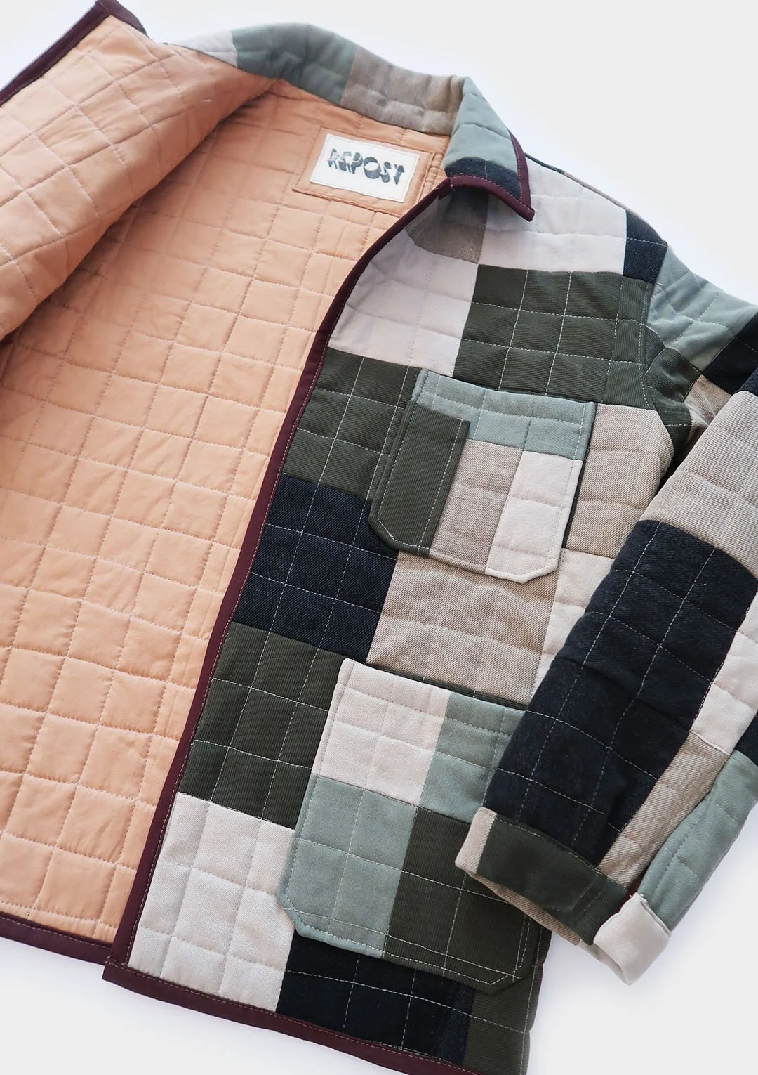 A patchwork quilted jacket with multiple plaid patterns in shades of beige, green, black, and gray, displayed on a flat surface.