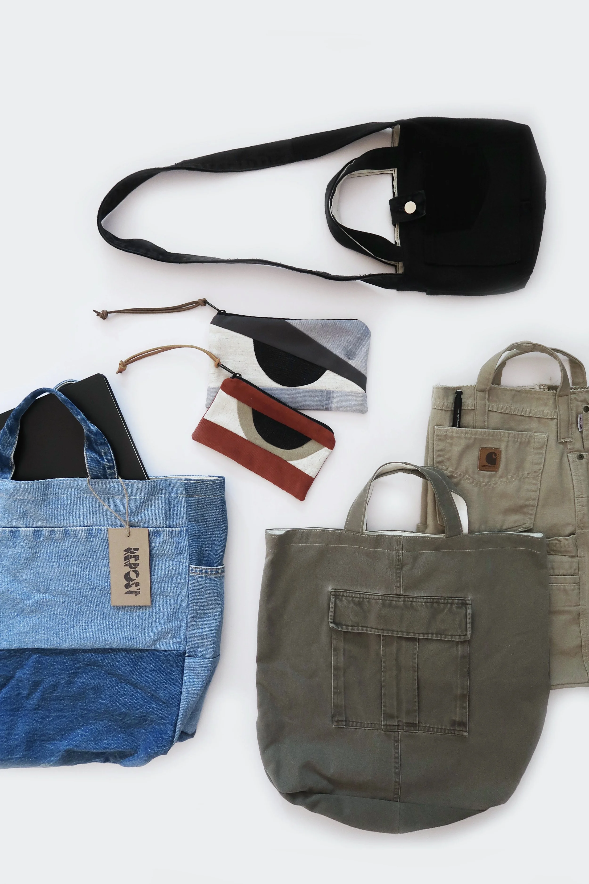 Various bags including a black tote, beige tote, blue denim tote with a tag, red and beige small clutch, gray and black clutch, and beige backpack with a pen, arranged on a white surface.