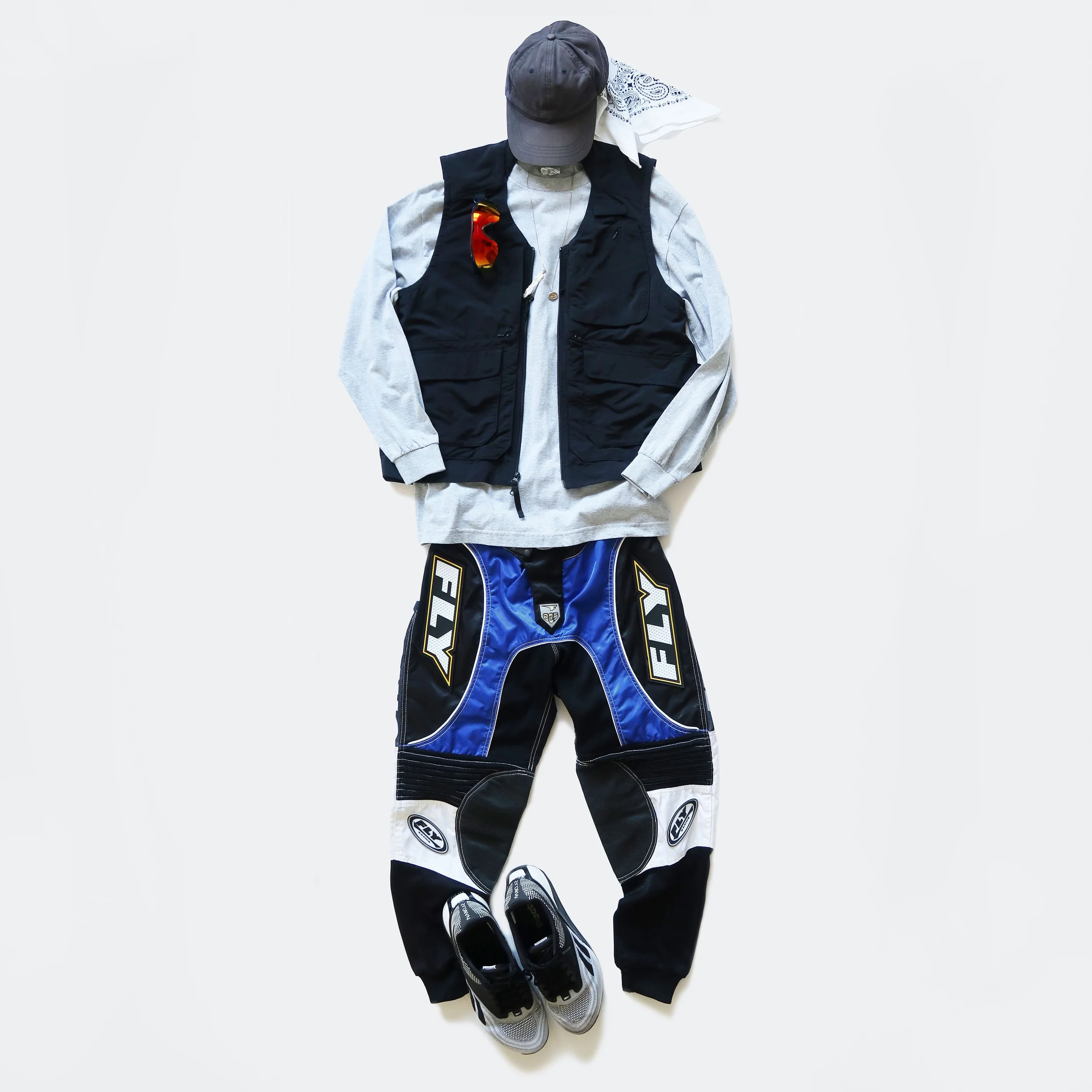 Sportswear and equipment including a gray cap, a black vest, a pair of sports shoes, and motocross pants arranged on a white background.