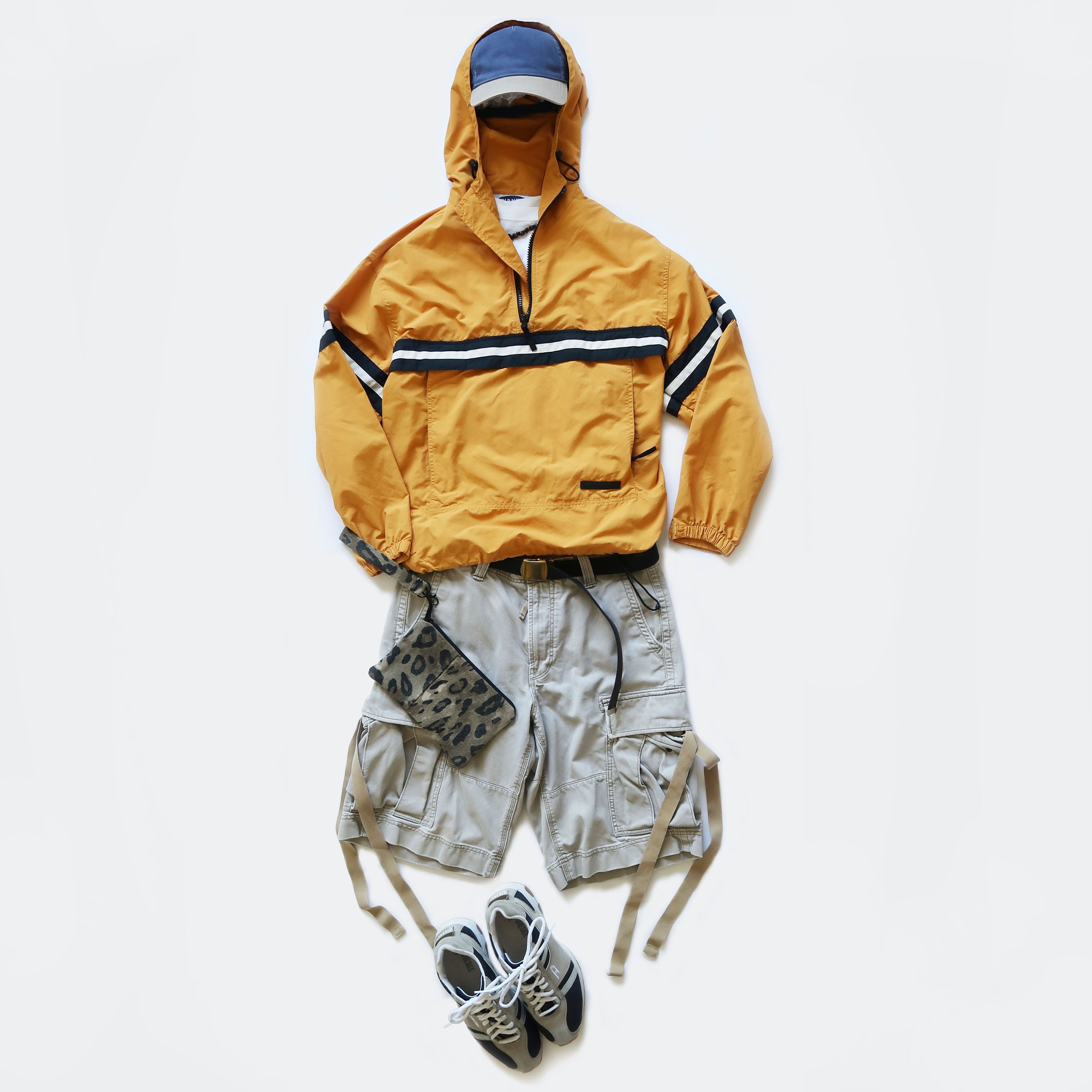A yellow and black jacket with a hood, a white and black pair of sneakers, beige shorts, and a leopard print face mask arranged on a white background.