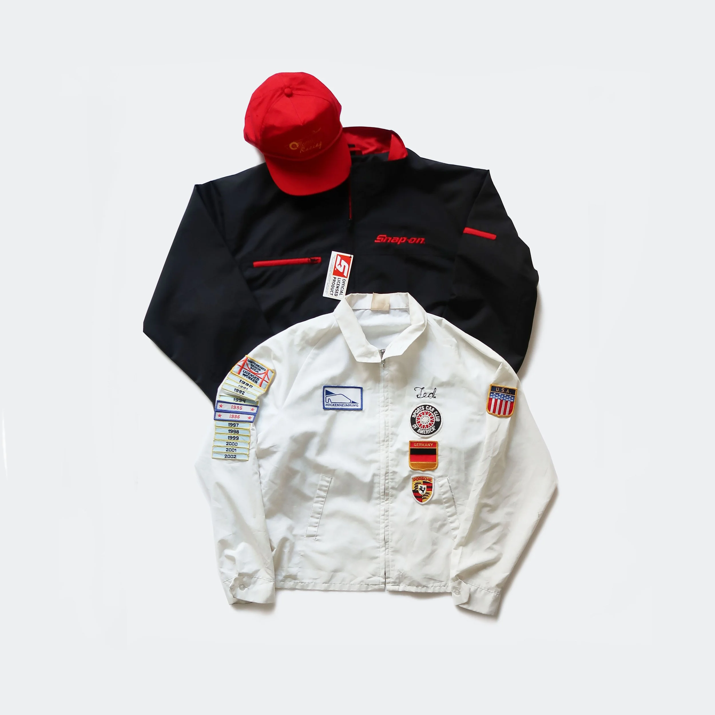 A collection of racing jackets and hats, including a white jacket with patches, a black jacket with red details, and a red cap.