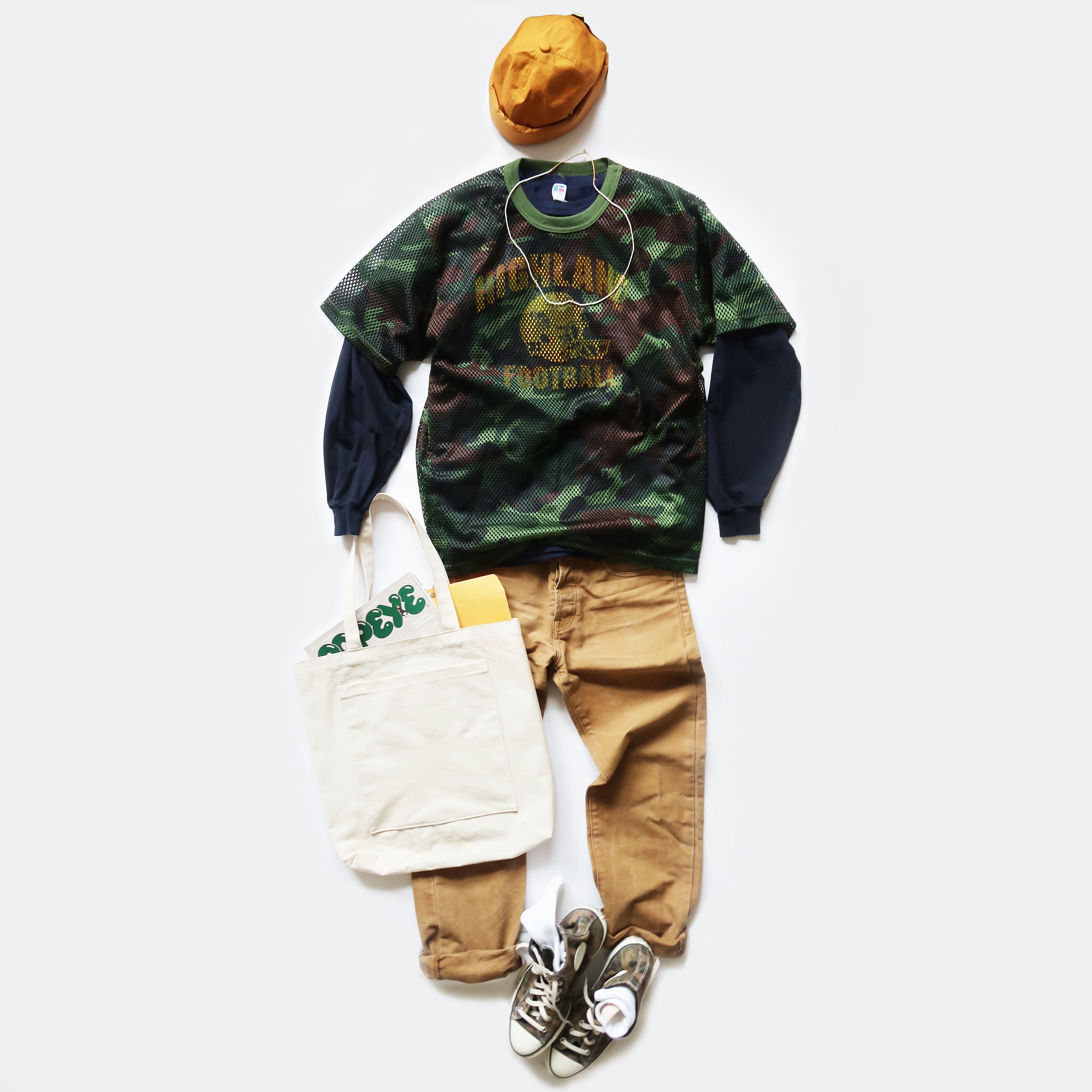 Casual clothing and accessories arranged on a white background, including a yellow hat, a camouflage-patterned t-shirt, tan pants, gray and white sneakers, and a white tote bag with a green design.