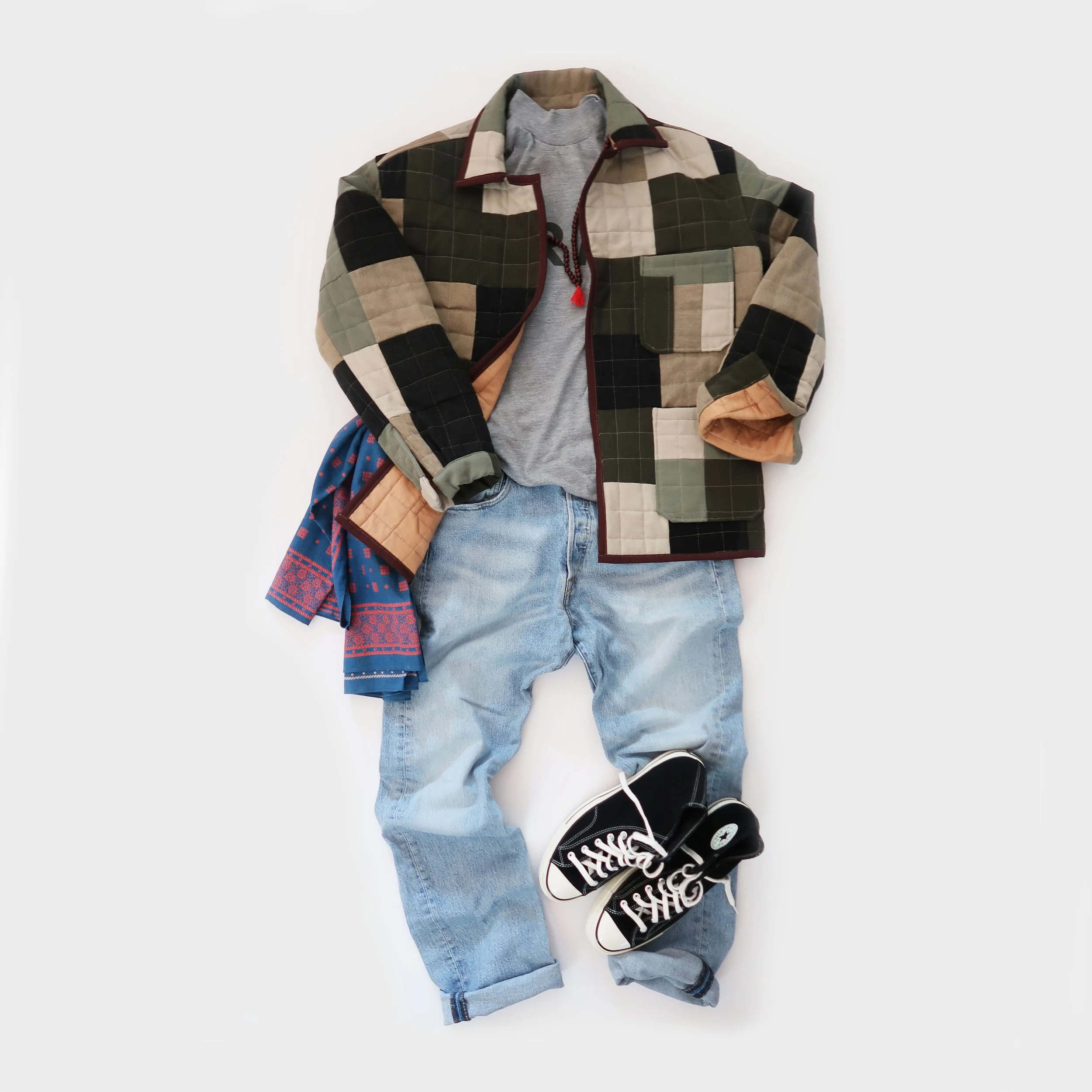 Flat lay of casual clothing including a plaid jacket, gray hoodie, blue jeans, and black sneakers with white soles on a white background.