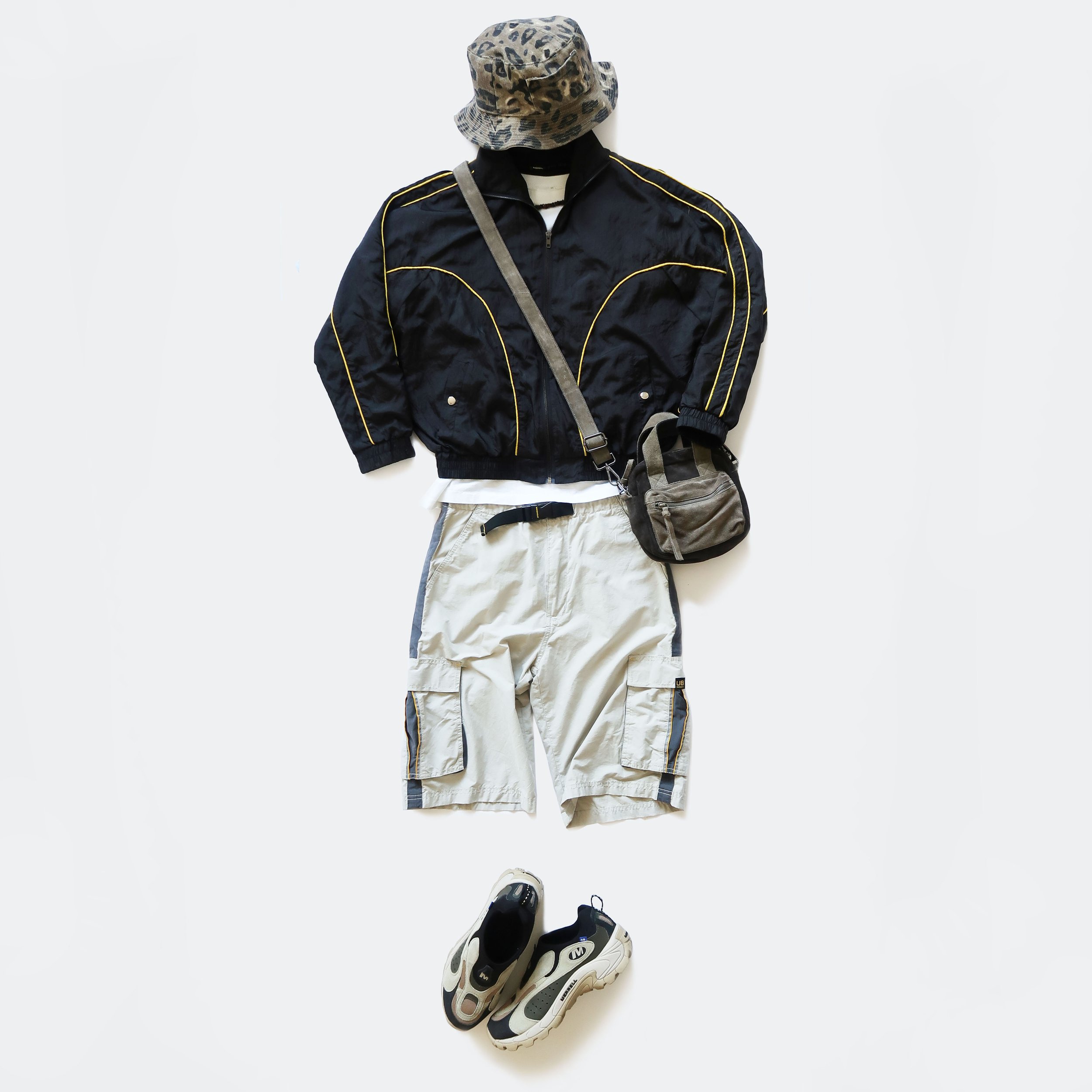 Casual outfit on a mannequin including a leopard print hat, black zip-up jacket with yellow piping, beige cargo pants with black drawstrings, a shoulder bag, and a pair of black and white athletic shoes.