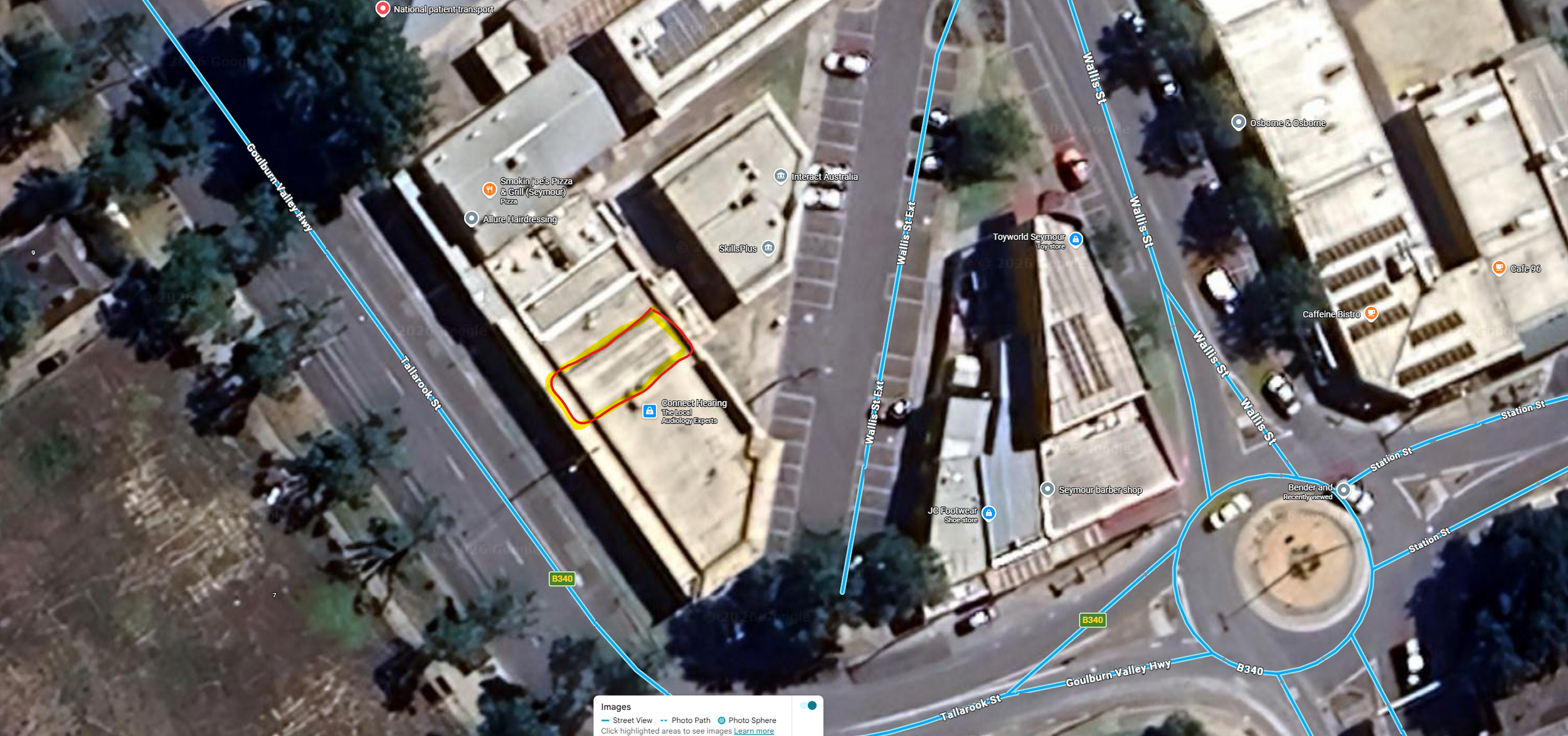 Aerial view of an urban area with streets, buildings, parking lots, and a circular roundabout, with a highlighted road segment outlined in red and yellow.