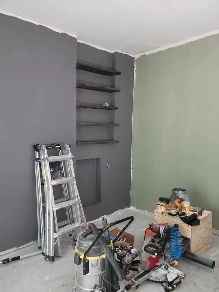 Room under renovation with a ladder, shelf, and tools scattered on the floor.