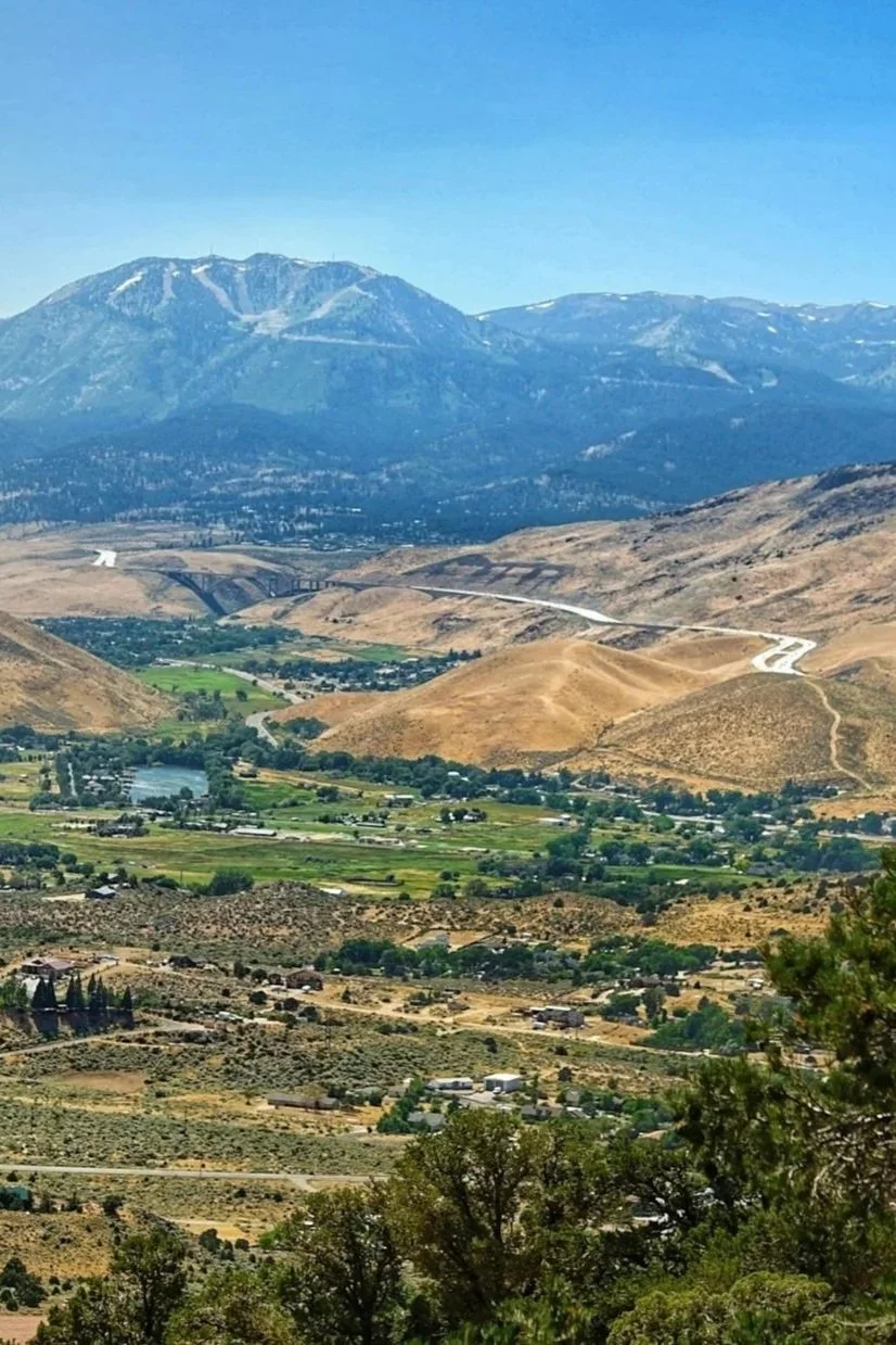 Scenic view of a the mountains surrounding Reno, NV with hills in the middle ground, and a valley with greenery and buildings in the foreground.