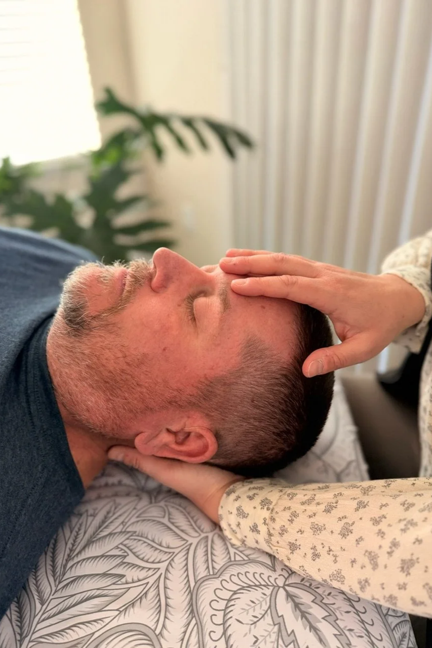 A person receiving a gentle CranioSacral Therapy treatment, with eyes closed, lying on a massage table.